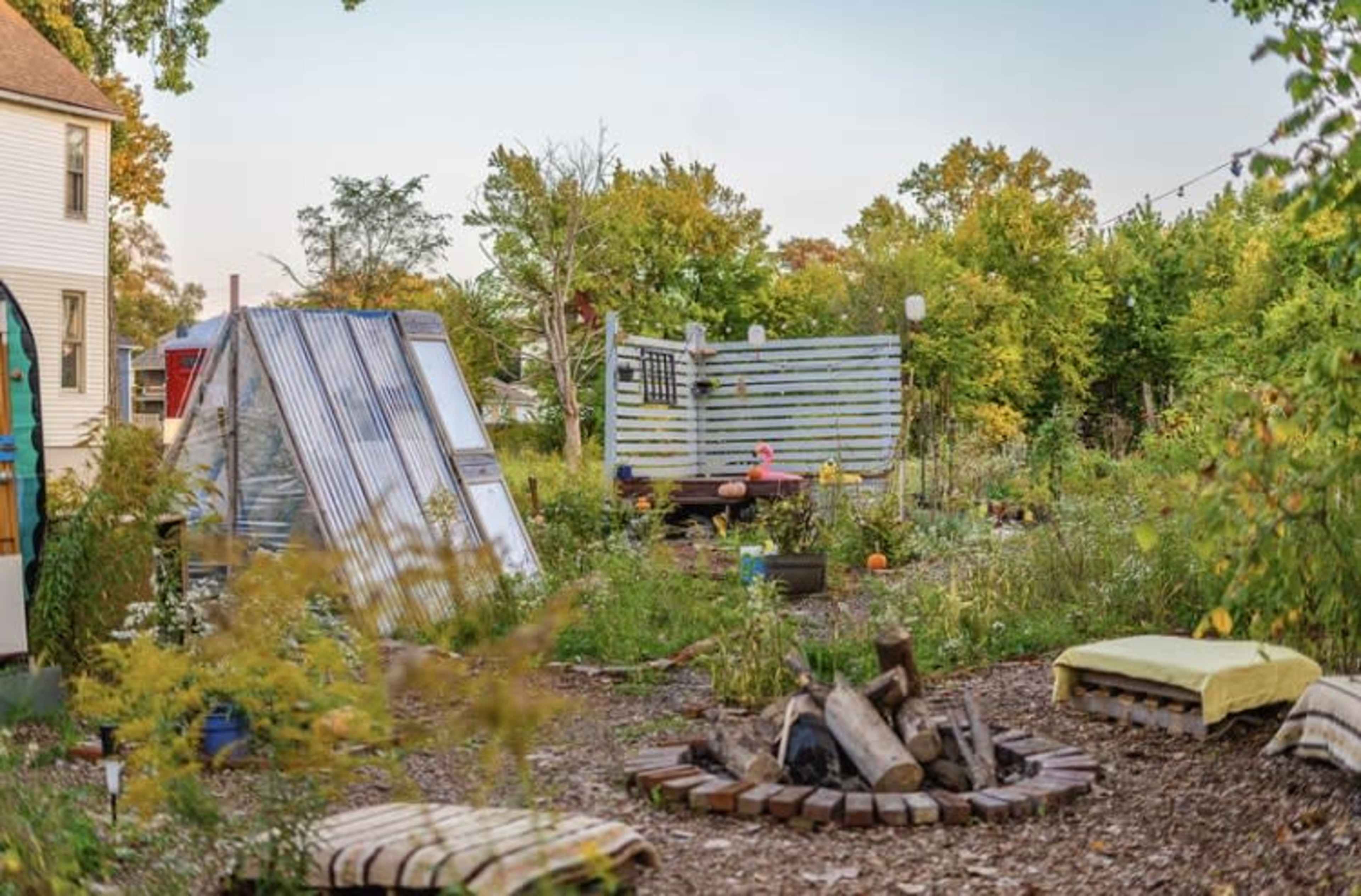 A community garden features raised beds, seating areas, and a small fire pit surrounded by greenery.