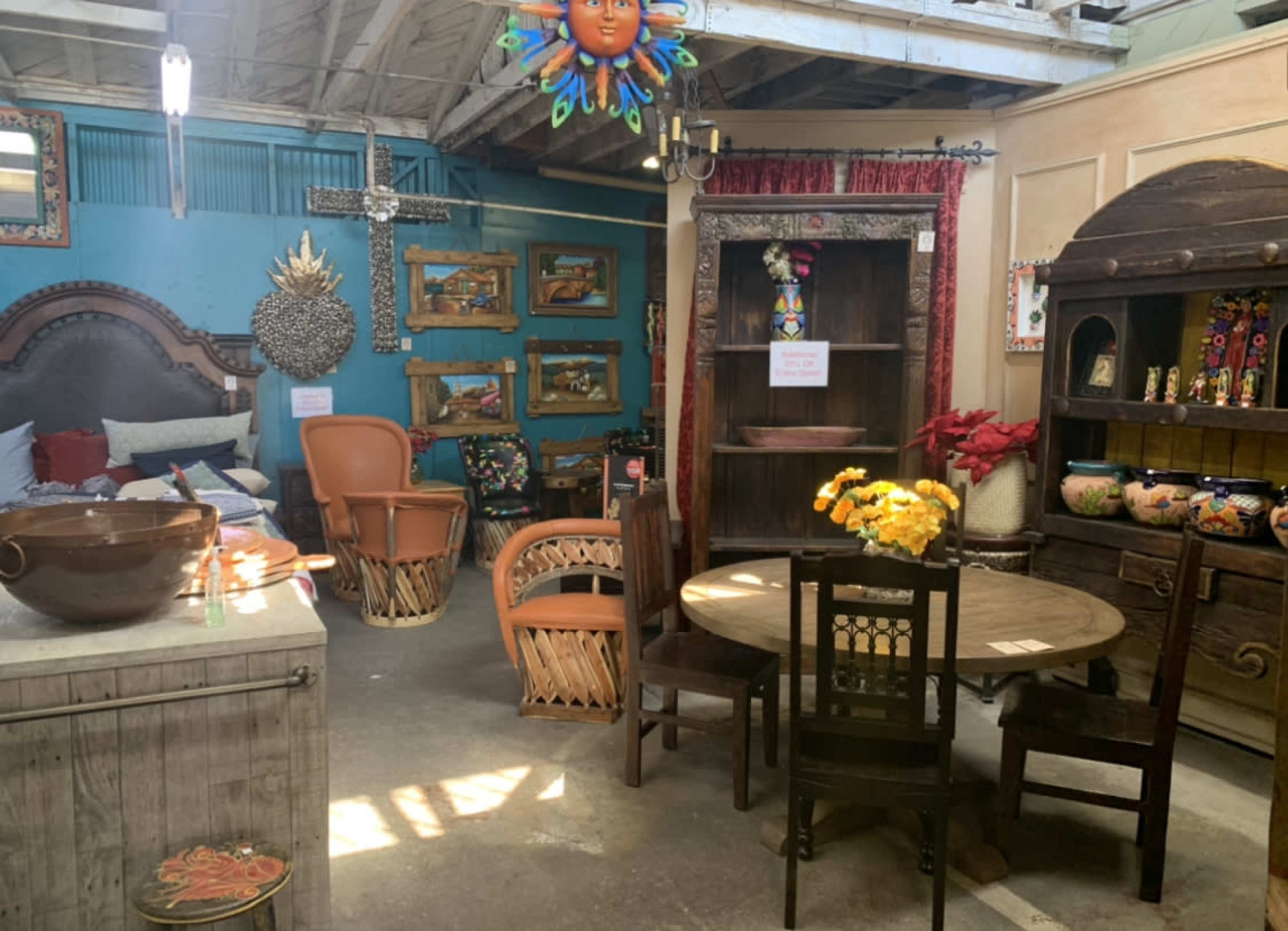 The image shows a cozy interior scene featuring various pieces of rustic furniture, including a wooden table with chairs, a wicker chair, and decorative wall art.