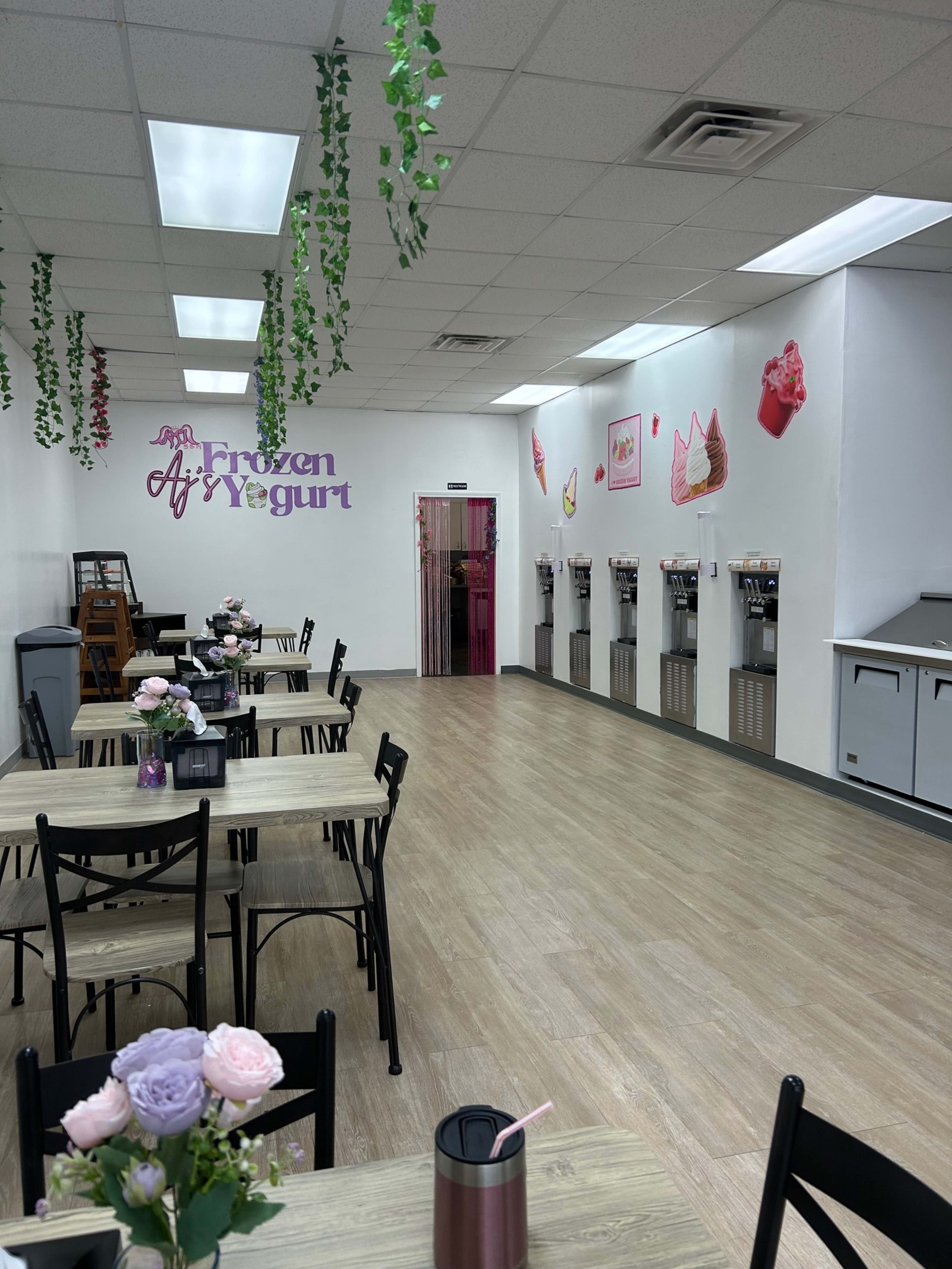 The image shows an interior of a frozen yogurt shop with tables, chairs, and several yogurt dispensers along the wall.