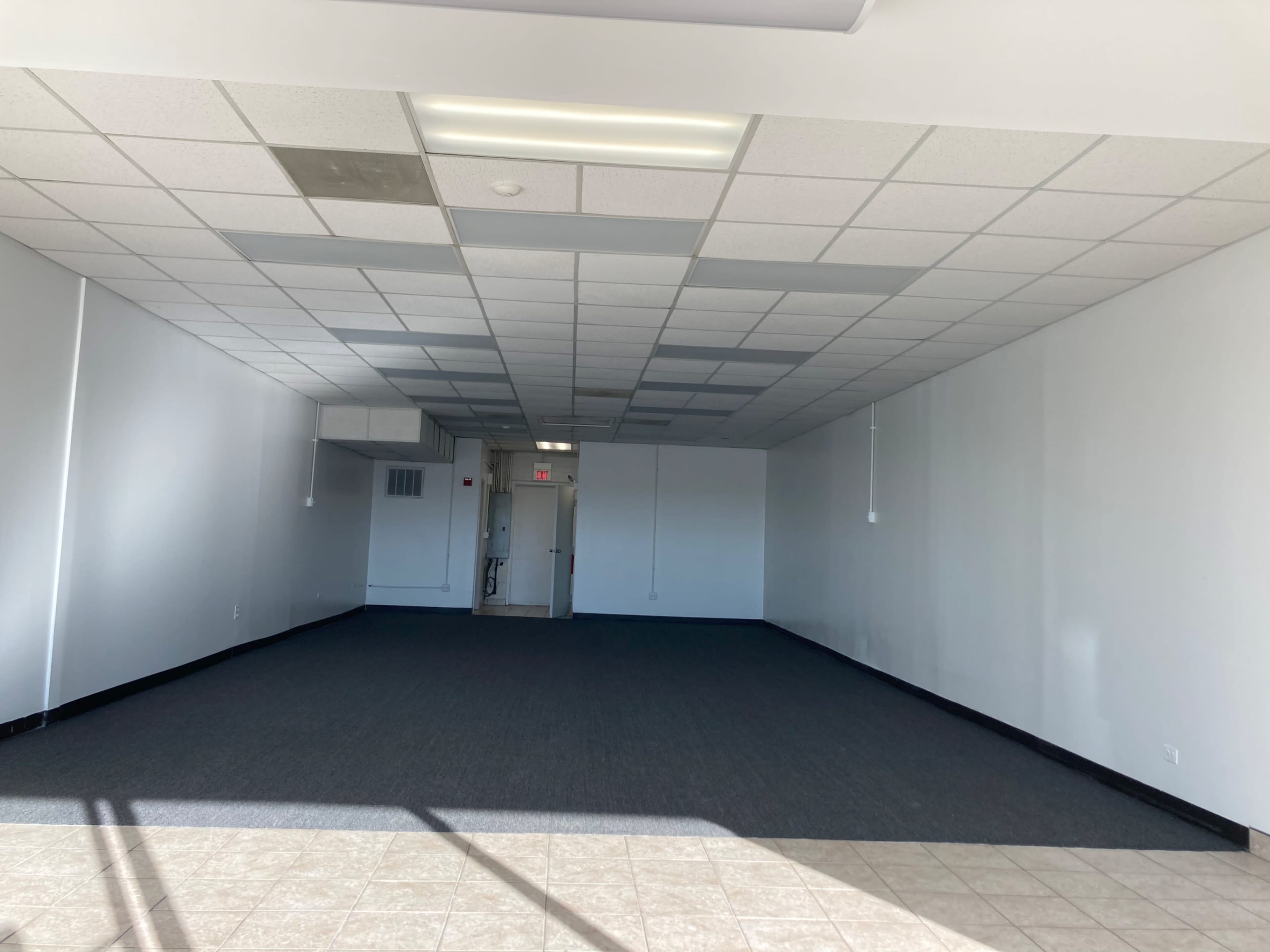 A vacant room with gray carpeting, white walls, and a doorway at the back.