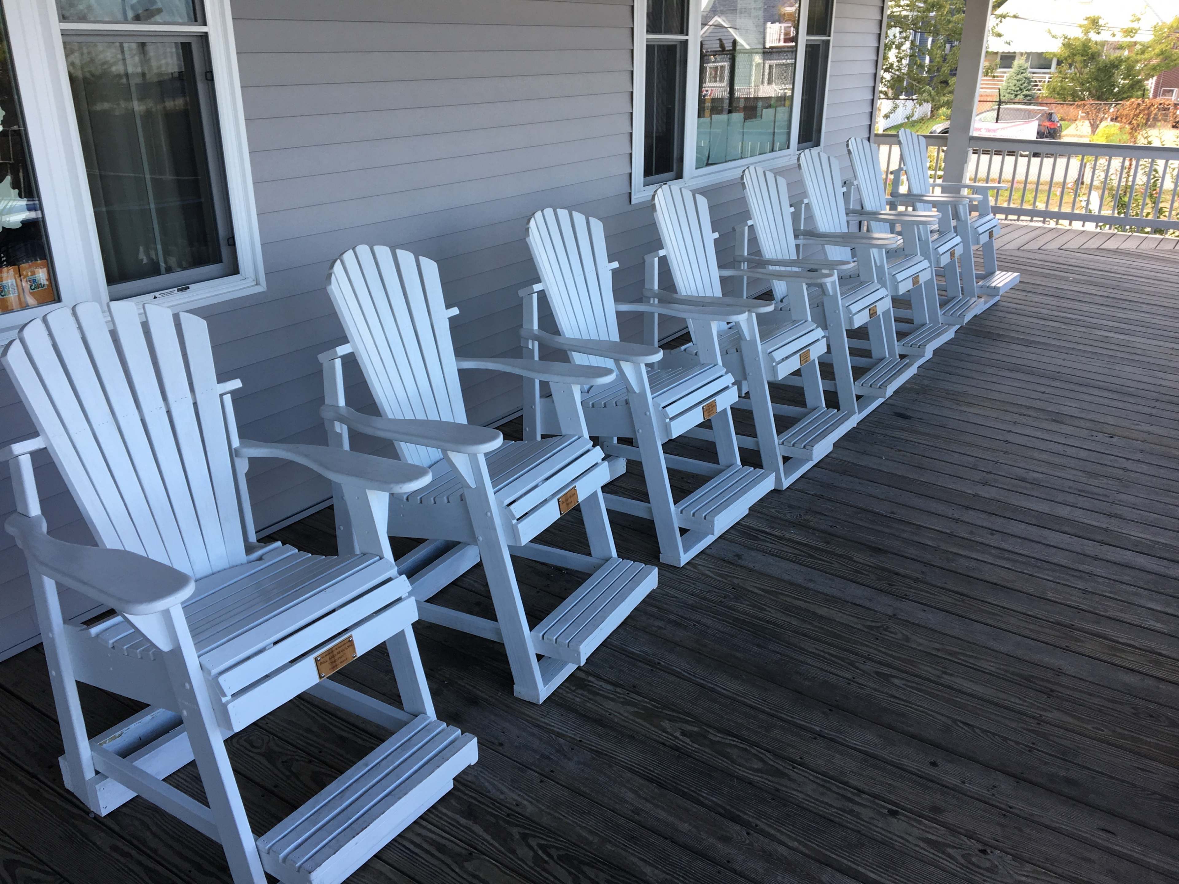 A row of white Adirondack chairs is lined up on a wooden deck.