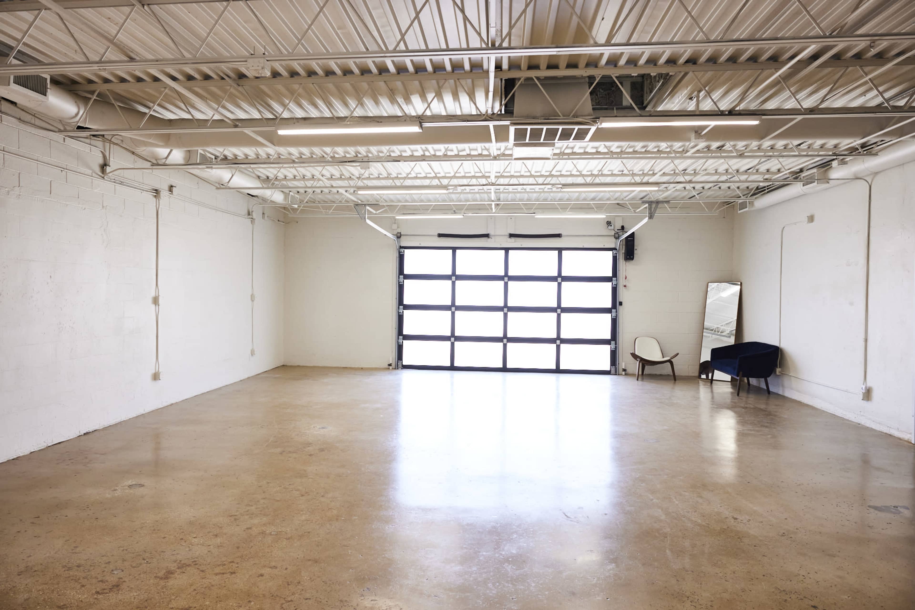 A spacious, empty garage with a large glass door and minimal furnishings, including a chair and a mirror.