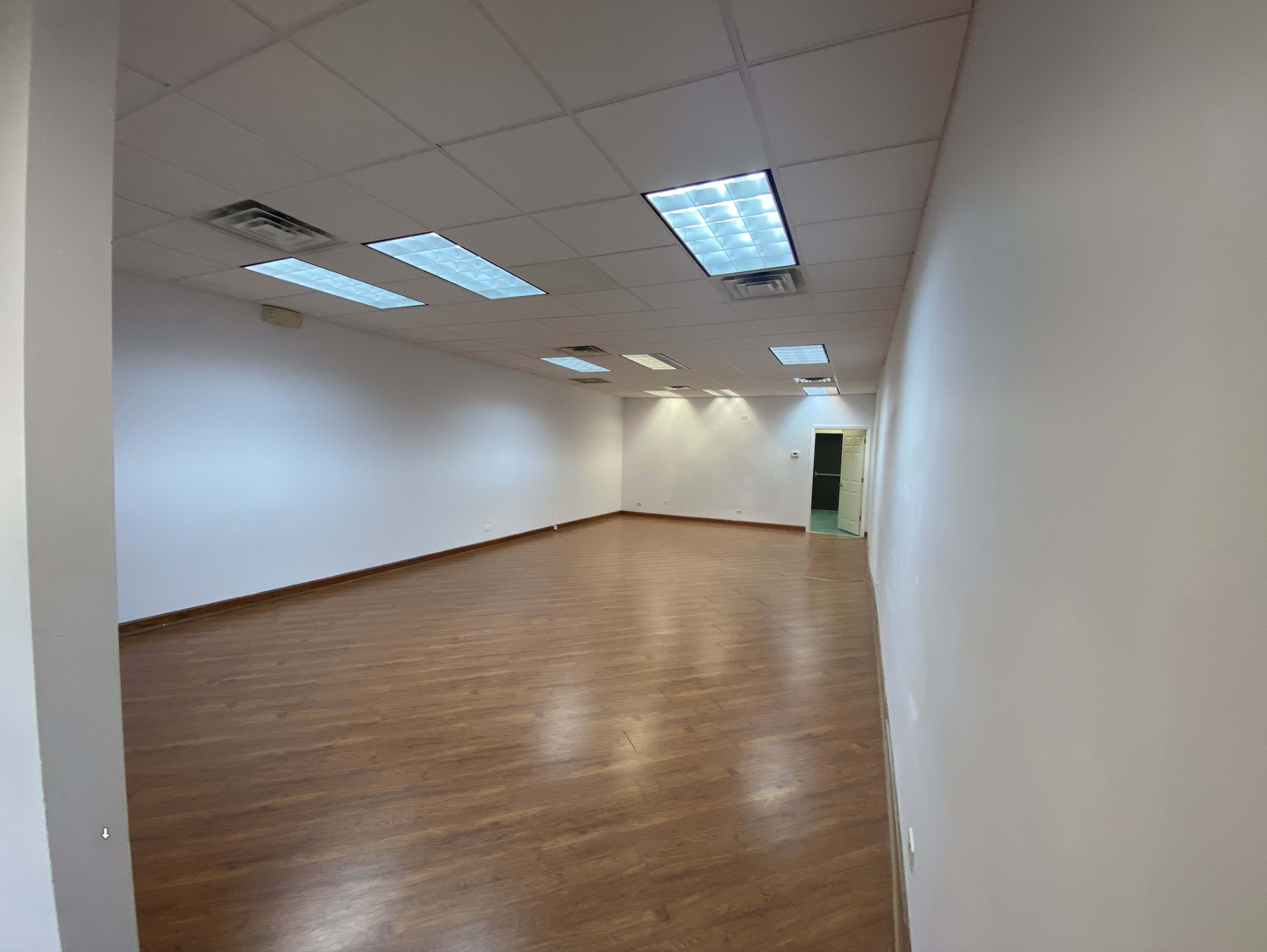 An empty room with wooden flooring, white walls, and fluorescent lighting.