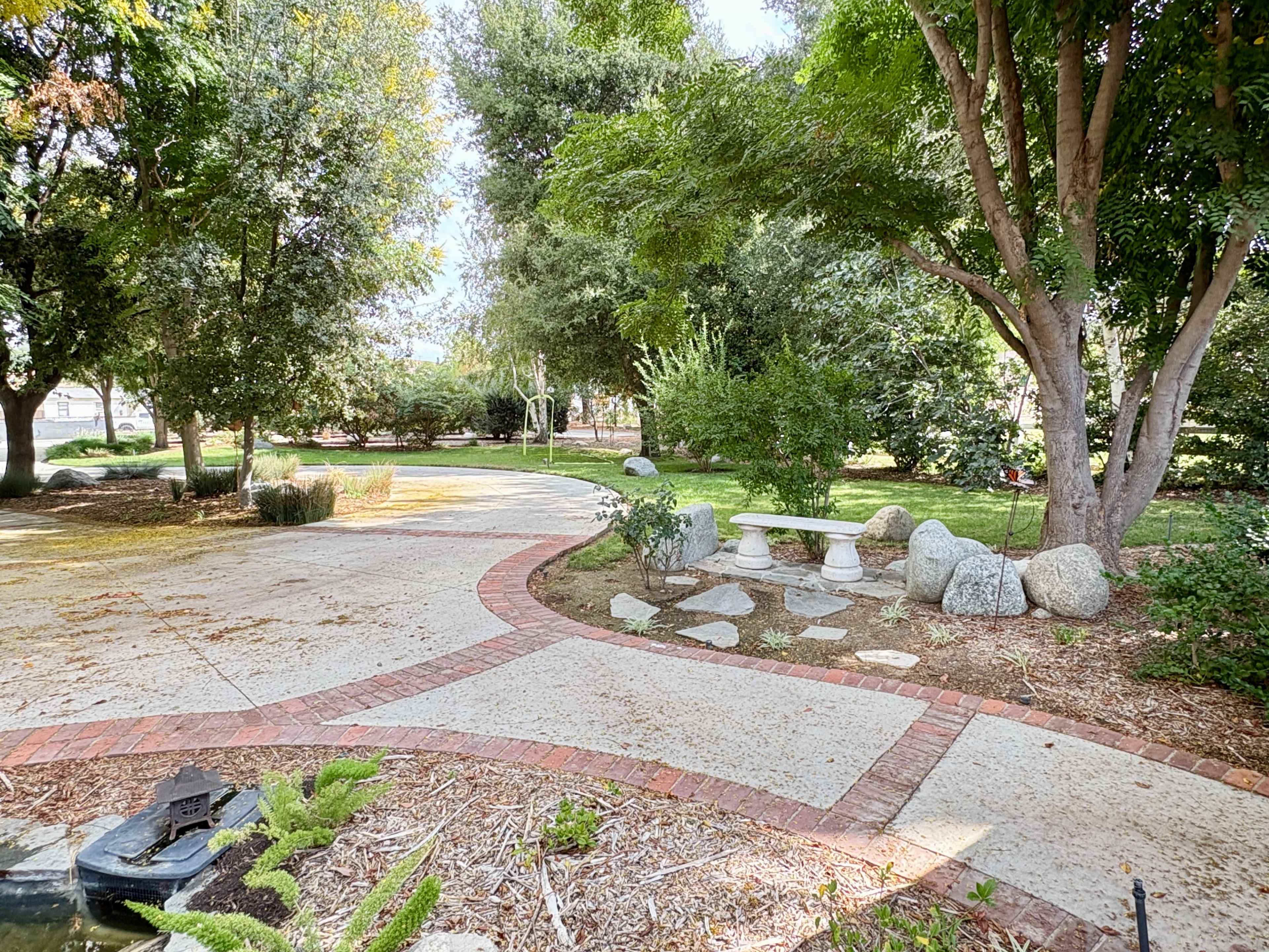 A winding pathway in a garden features a stone bench surrounded by trees and landscaped greenery.