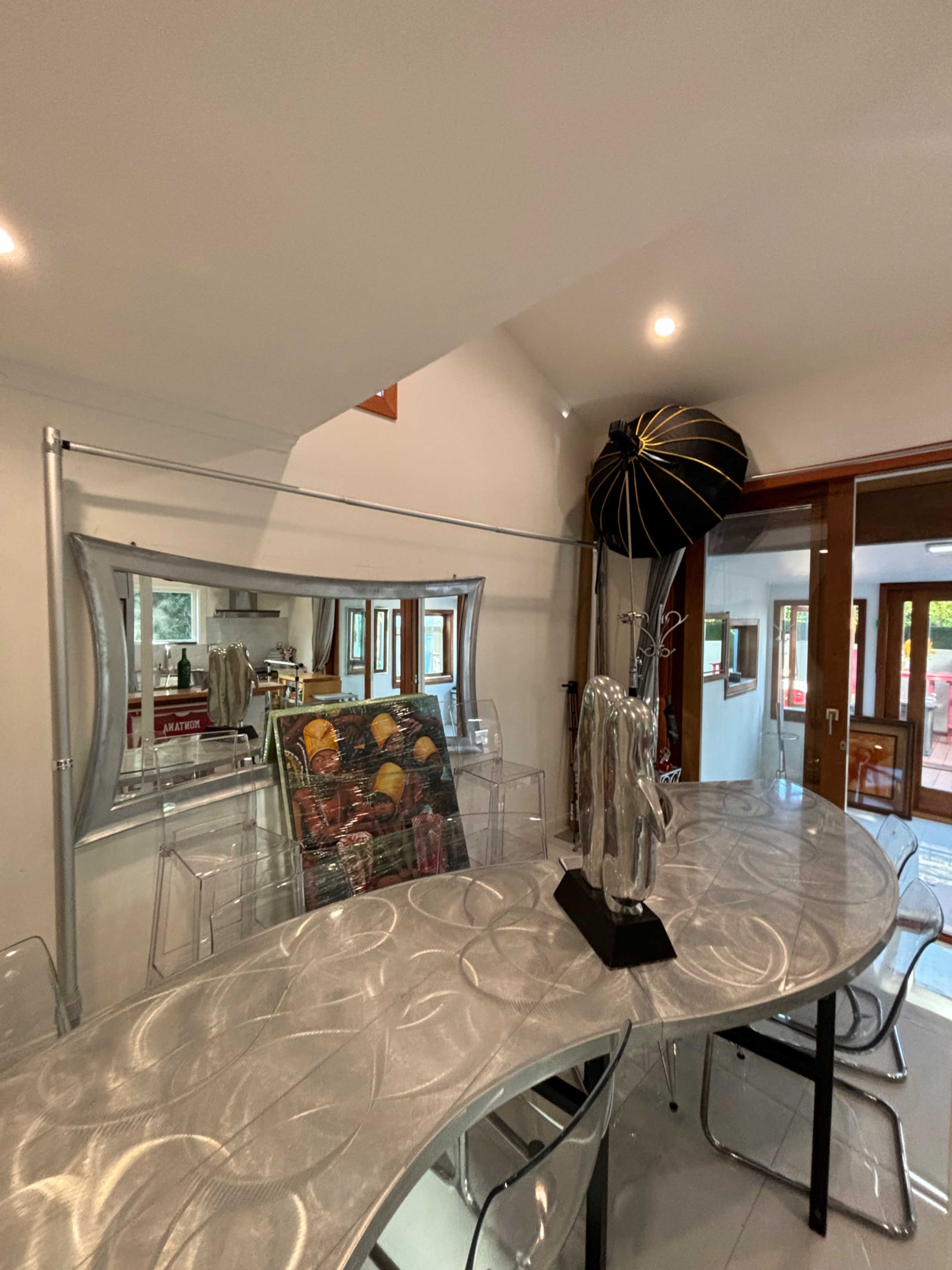 The image shows a modern dining area featuring a sleek oval table, clear chairs, a large mirror, and an umbrella-shaped decorative element in the background.