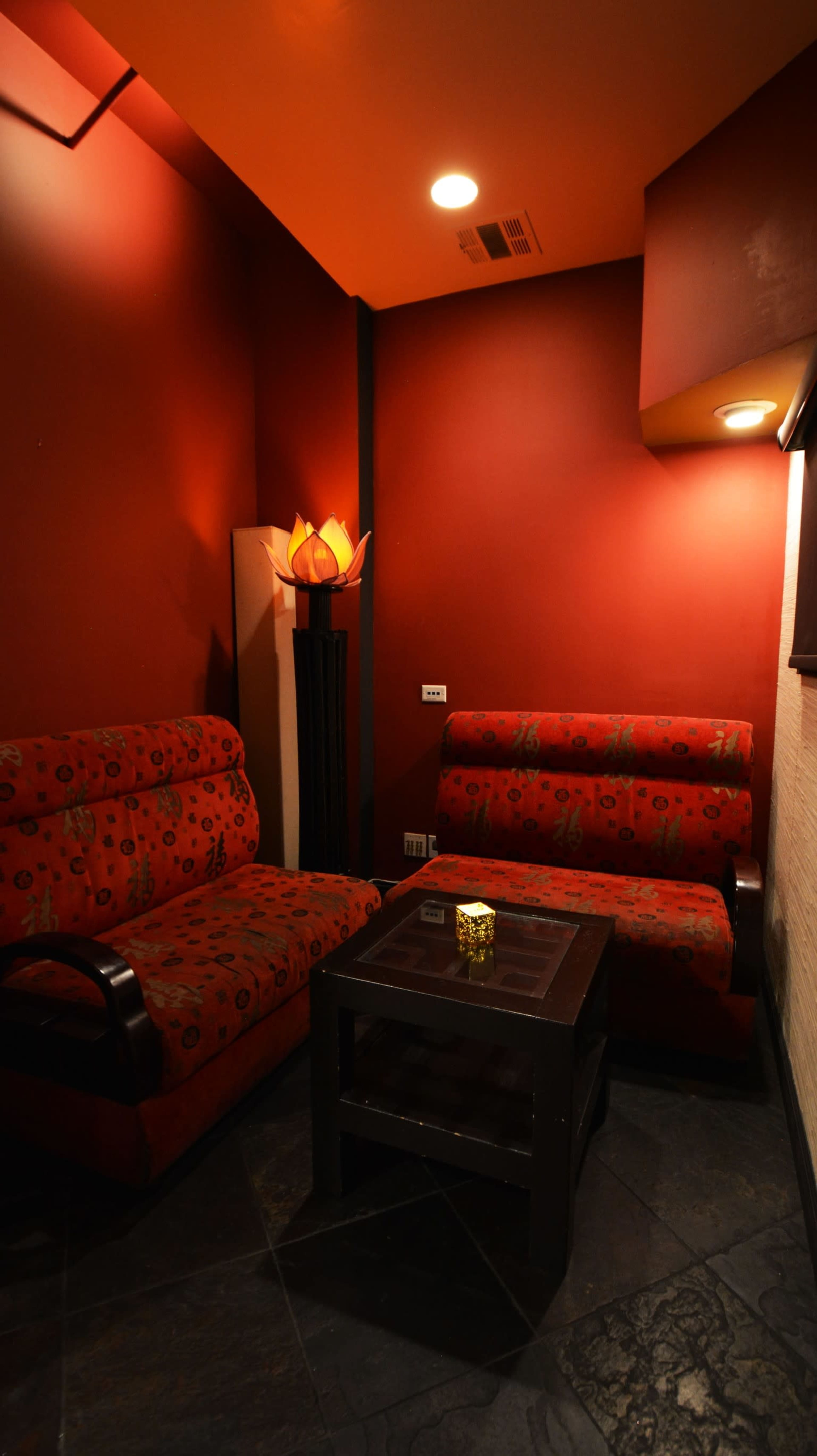 A cozy seating area features two patterned red chairs and a black coffee table, set against dark red walls and illuminated by warm lighting.