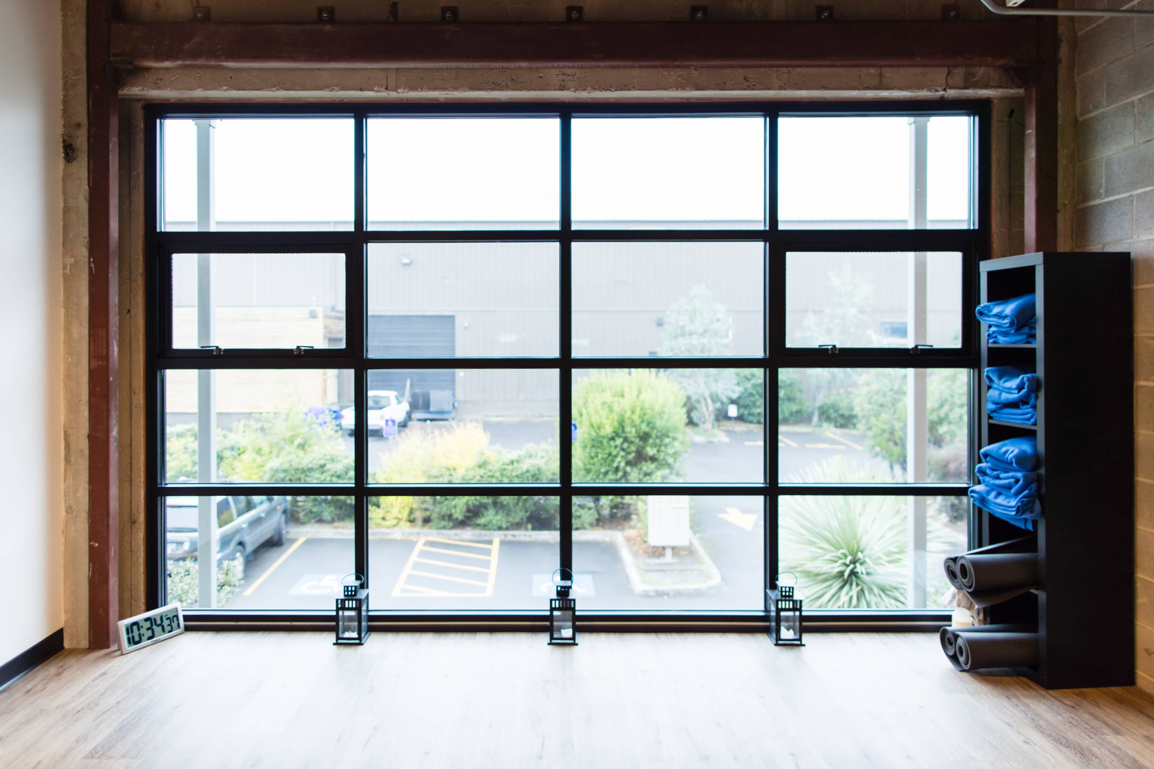 A large window with a grid pattern, revealing a view of an outdoor parking area and greenery, alongside a shelf holding neatly stacked blue towels and rolled mats.