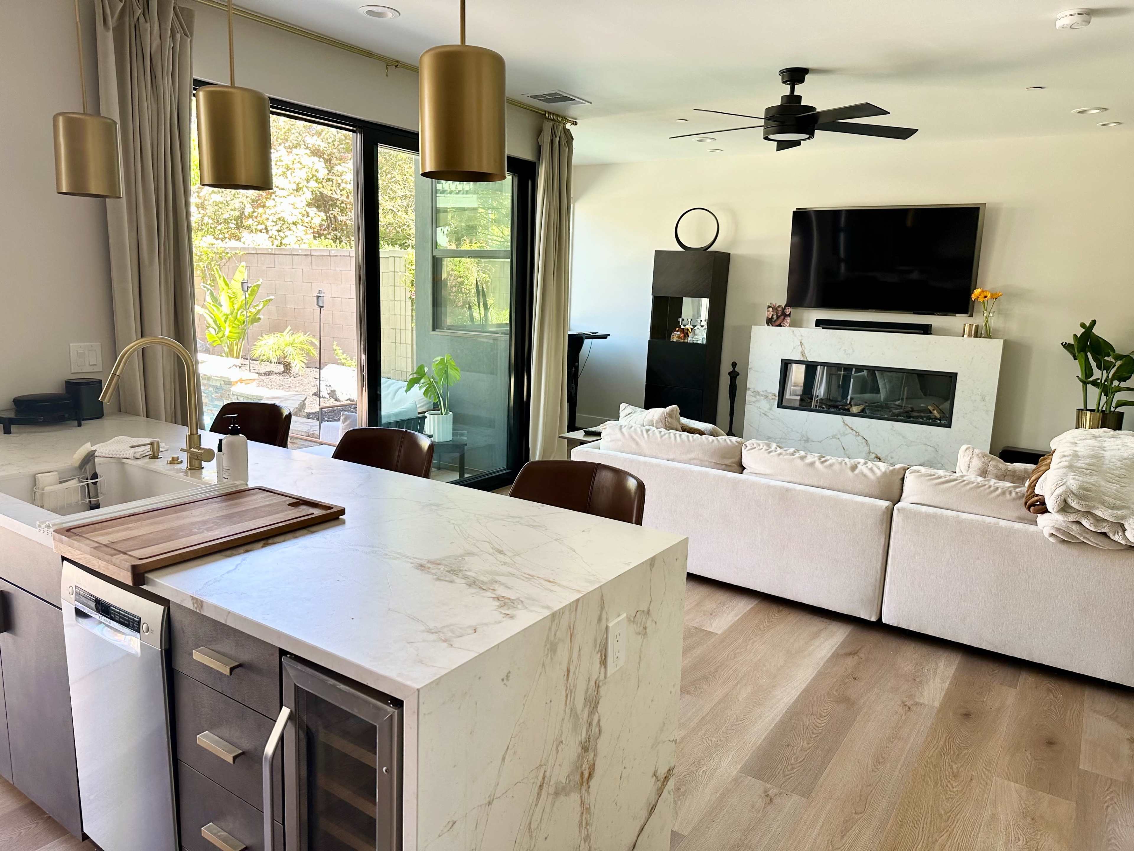 A modern living space featuring a kitchen with a marble countertop and an open layout connecting to a cozy living area with beige sofas.