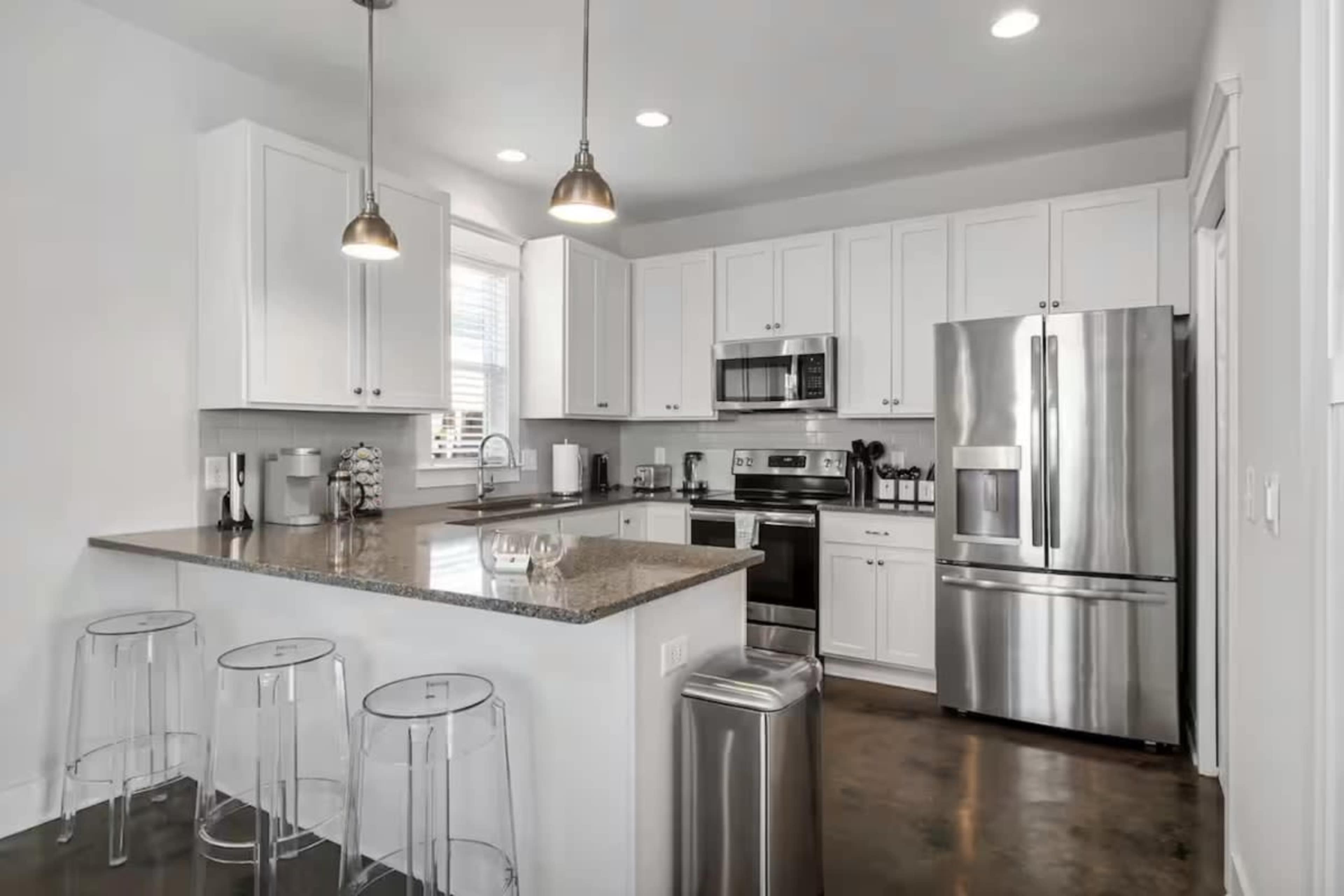 The kitchen features white cabinetry, stainless steel appliances, and a central island with clear acrylic stools.