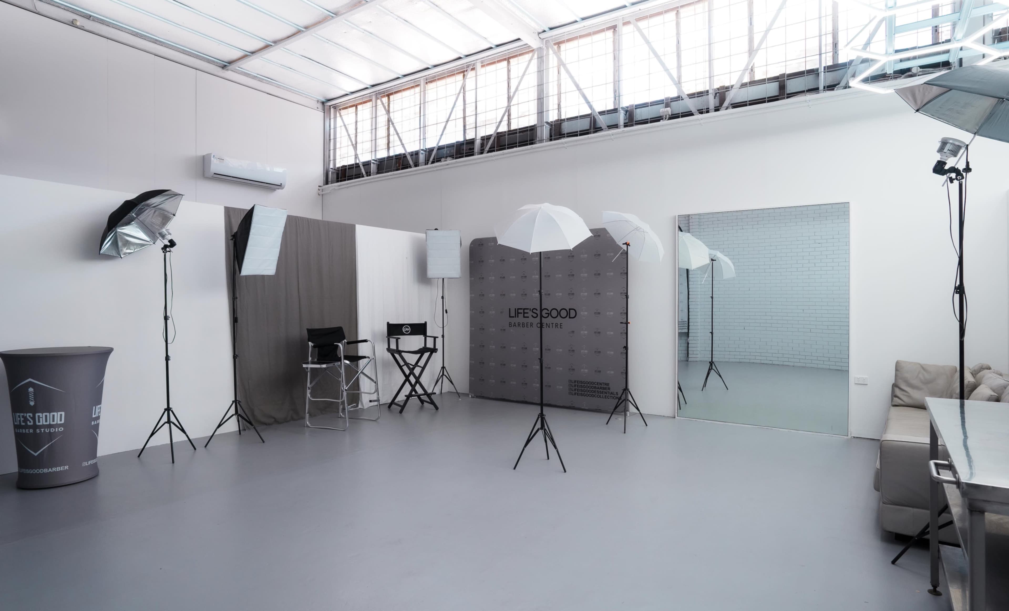 The image shows a photography studio equipped with lighting equipment, a director's chair, and a large mirror against a minimalist backdrop.