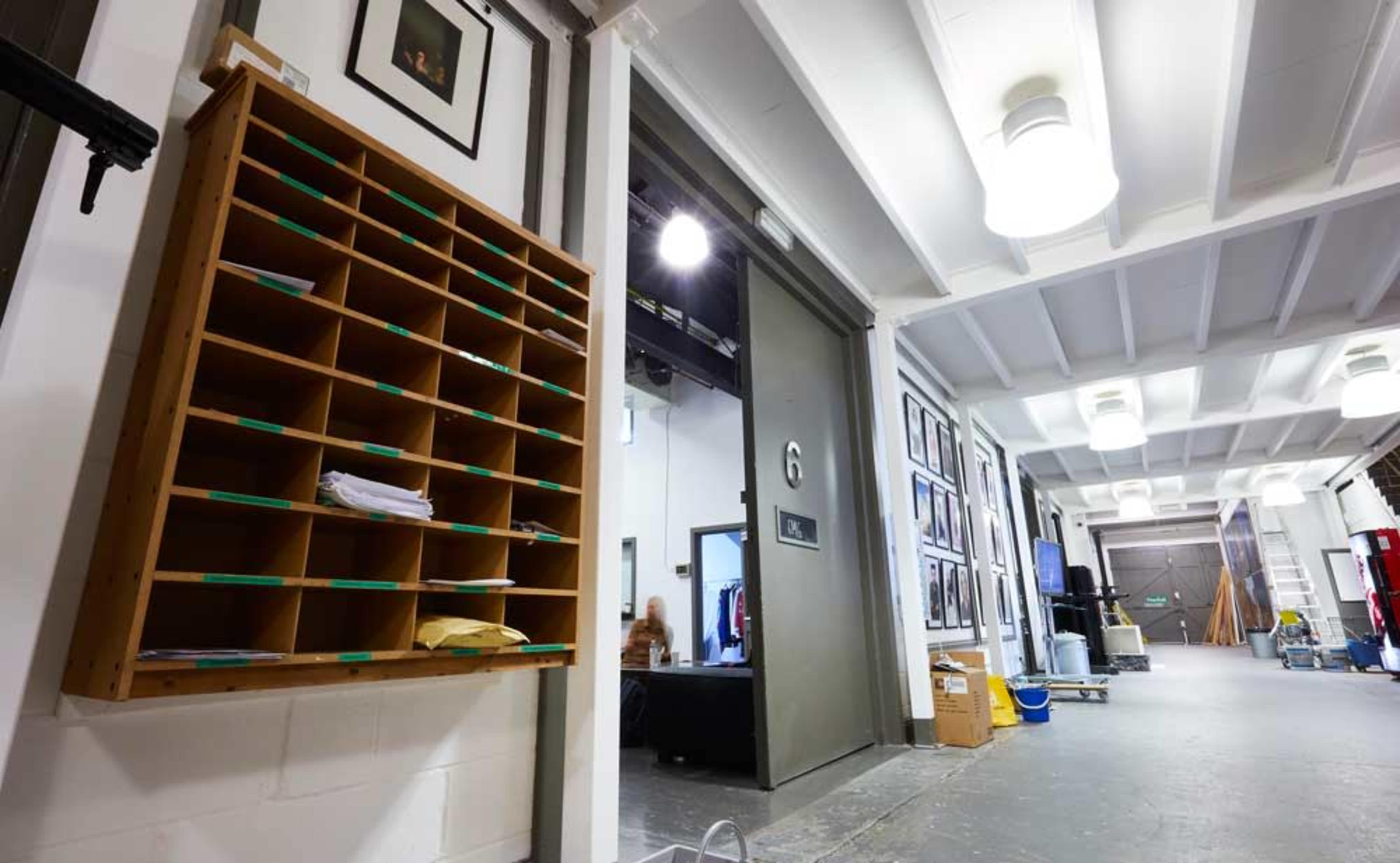 A hallway with a wooden mail organizer on the left and doors leading to other rooms on the right, along with various items scattered on the floor.