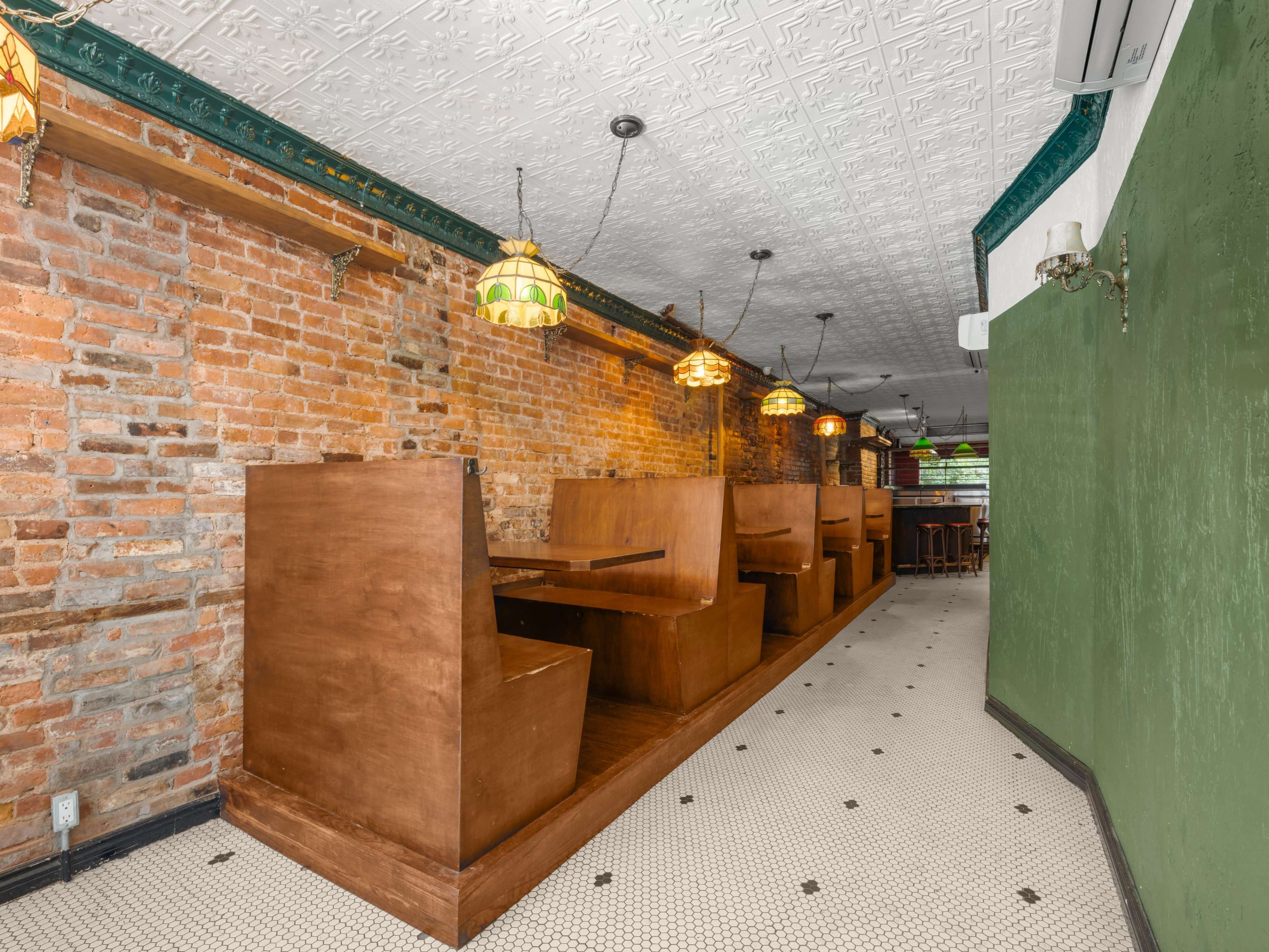 The image shows a narrow restaurant interior with wooden booths along one side, exposed brick walls, and vintage-style pendant lighting.