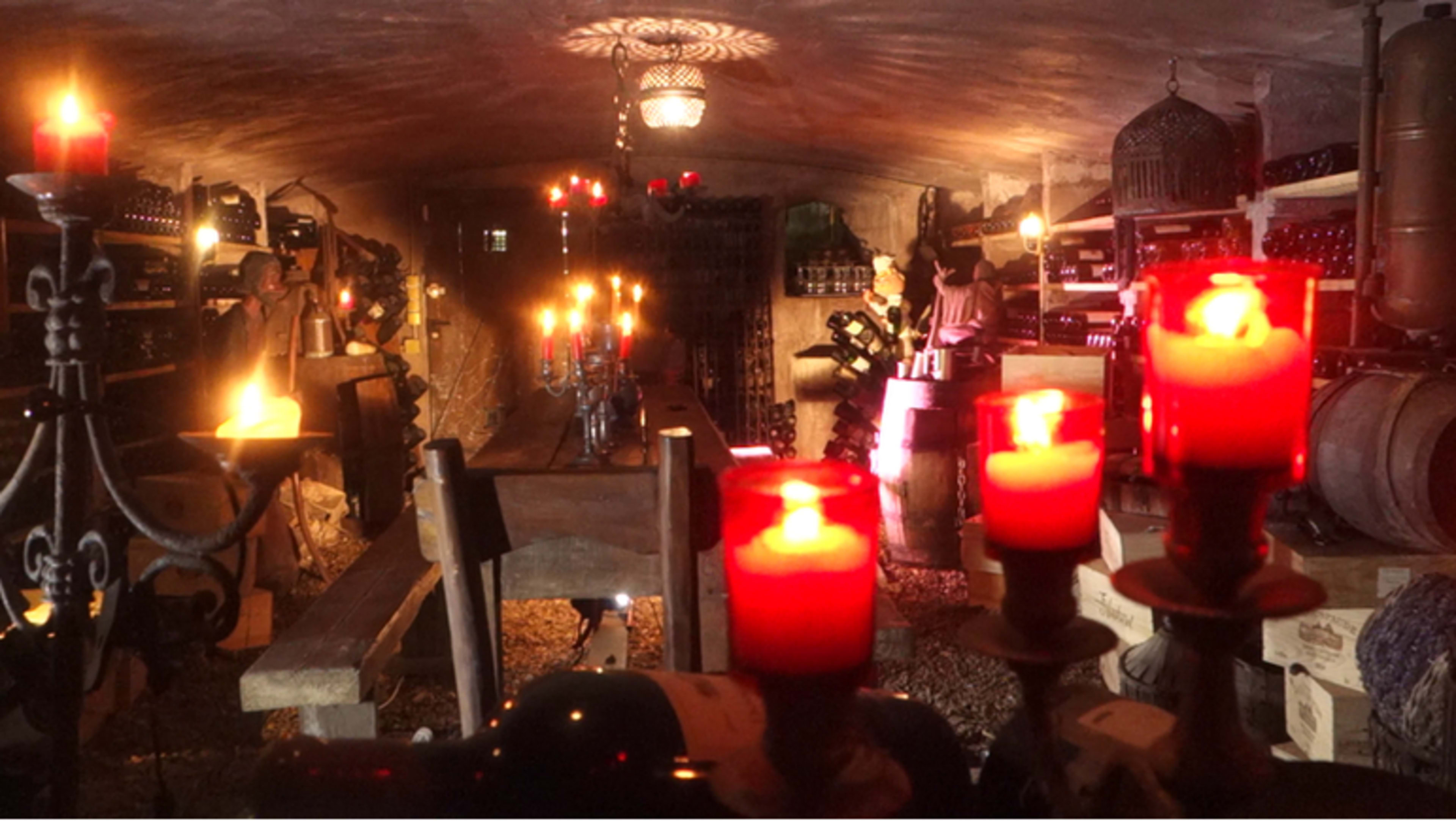 A dimly lit wine cellar adorned with candles, showcasing shelves filled with wine bottles and wooden barrels along the walls.
