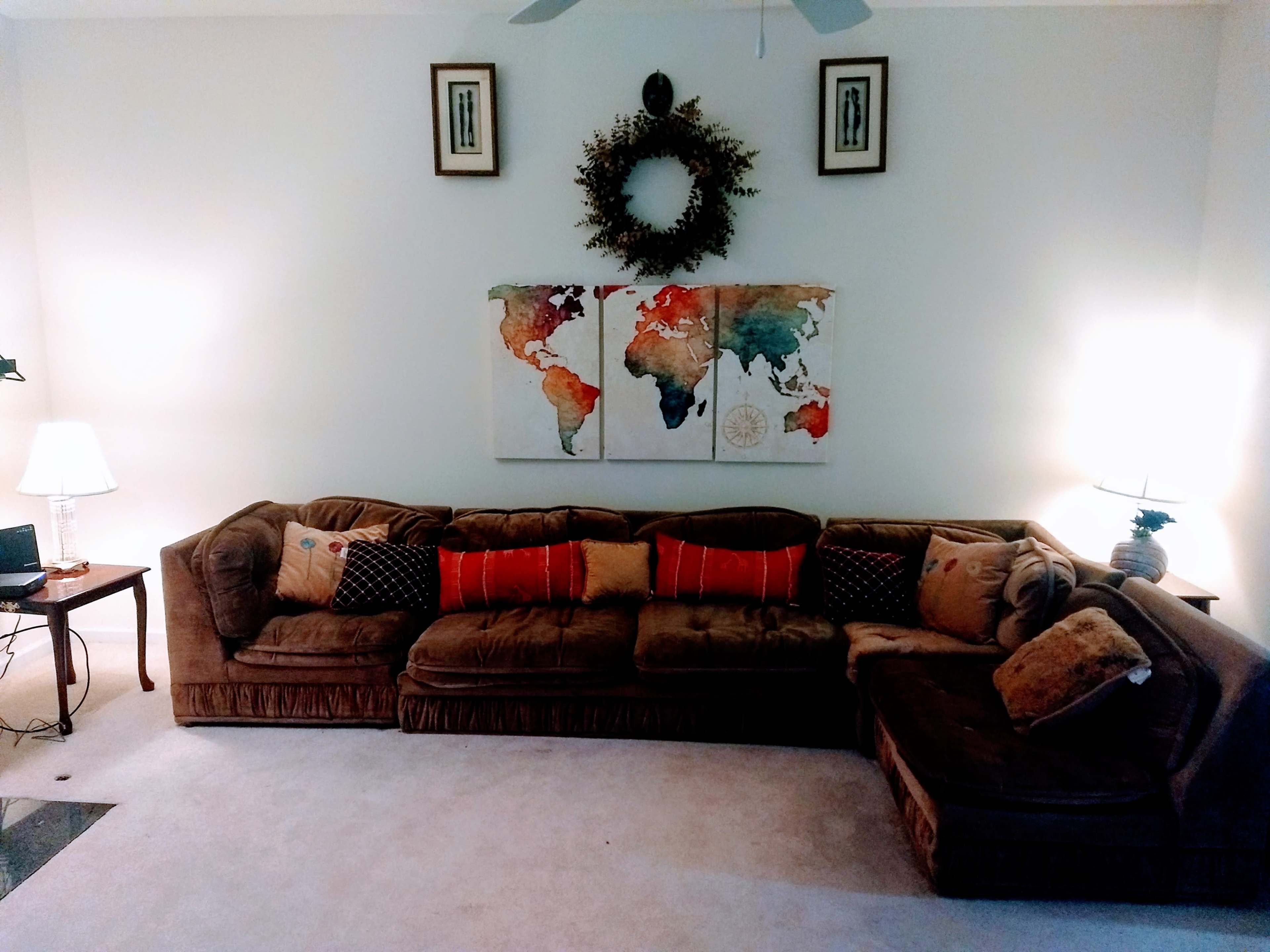 A brown sectional sofa with decorative pillows is positioned in a softly lit living room featuring a world map artwork and wall decor.