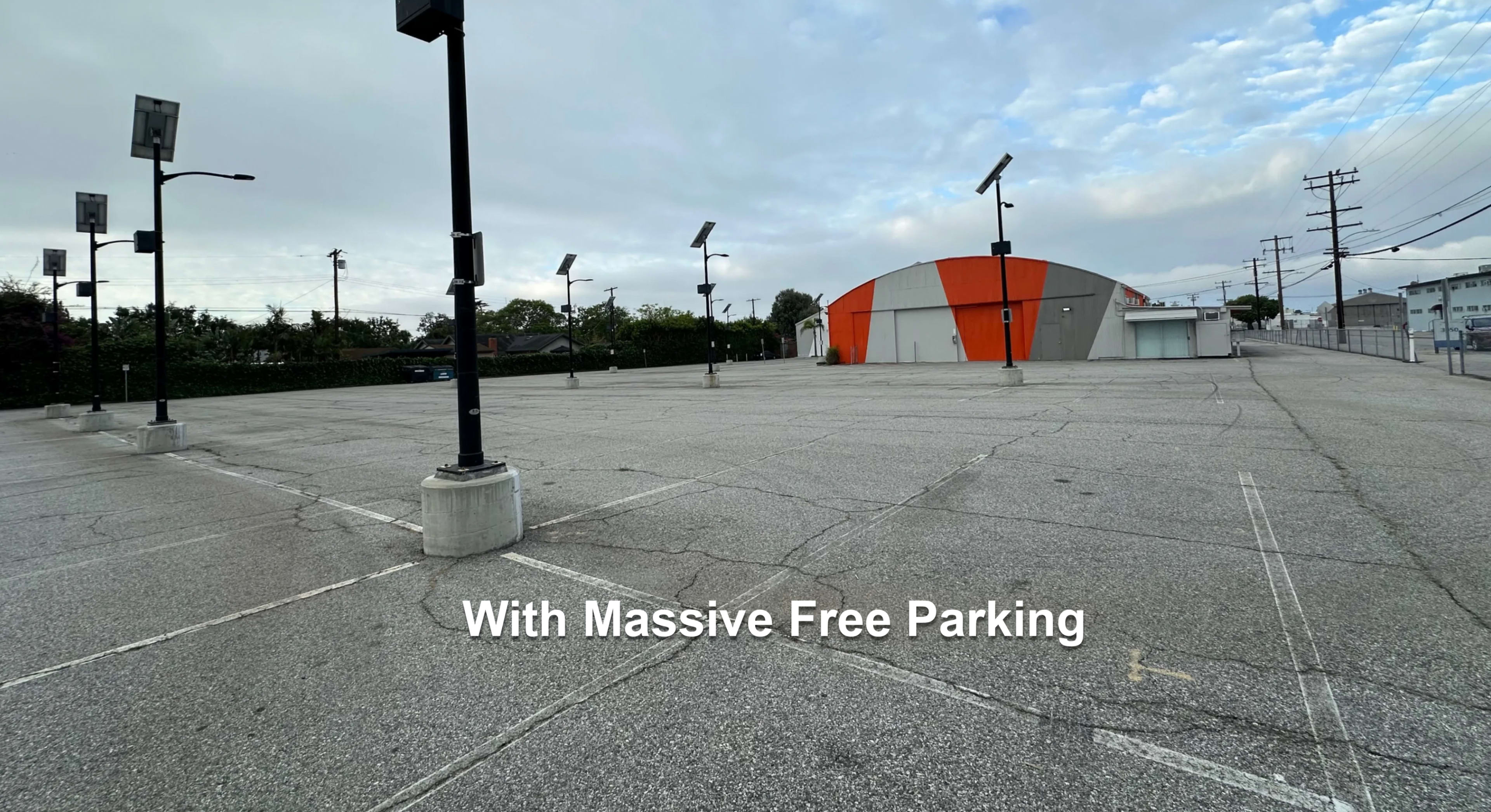 The image shows an empty parking lot with several light poles and a large building in the background featuring orange and gray architectural elements.