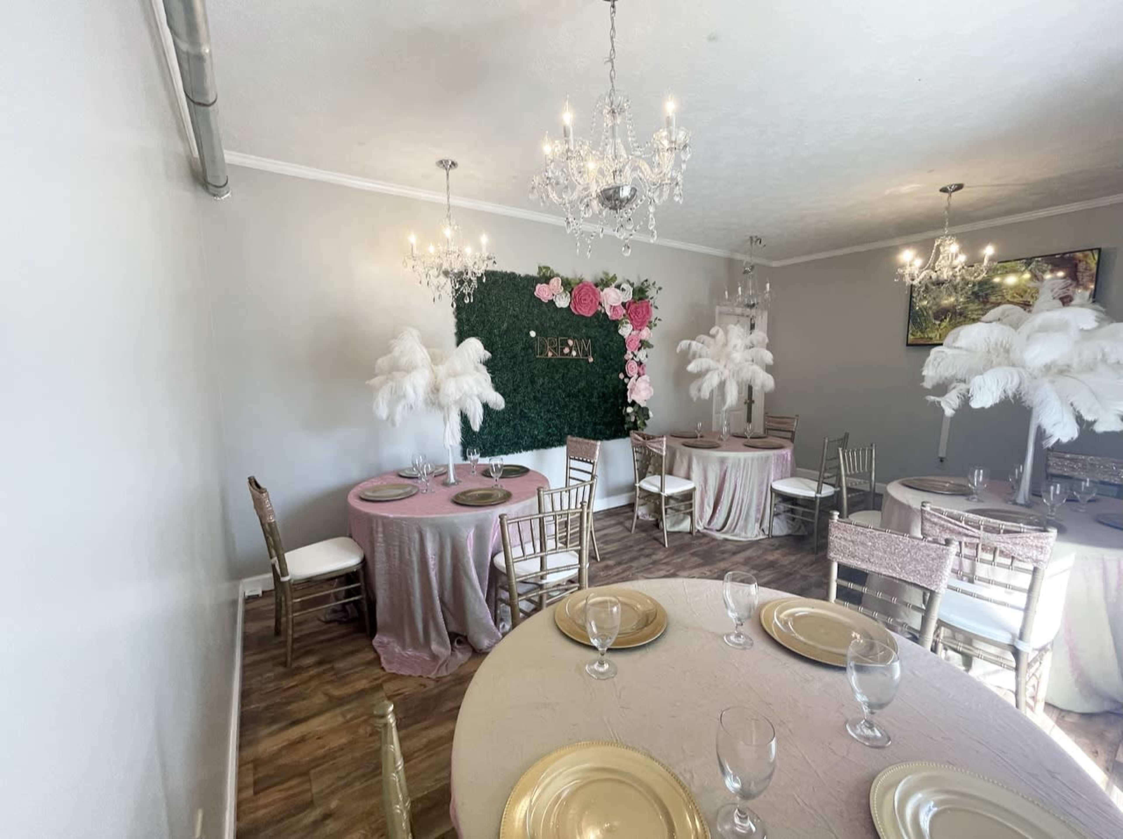 A decorated interior dining area featuring round tables with tablecloths, gold plates, and a green wall adorned with flowers.