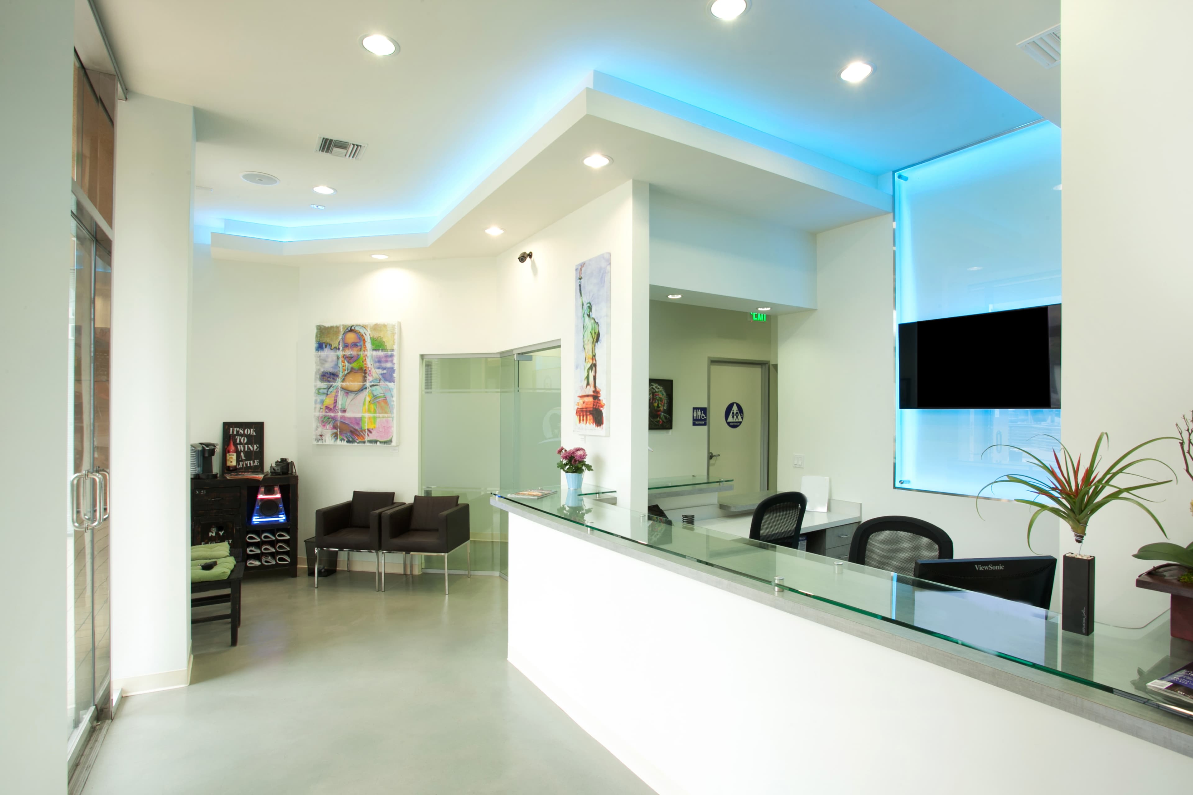 The image shows a modern reception area with a glass counter, seating area, and decorative artwork on the walls.