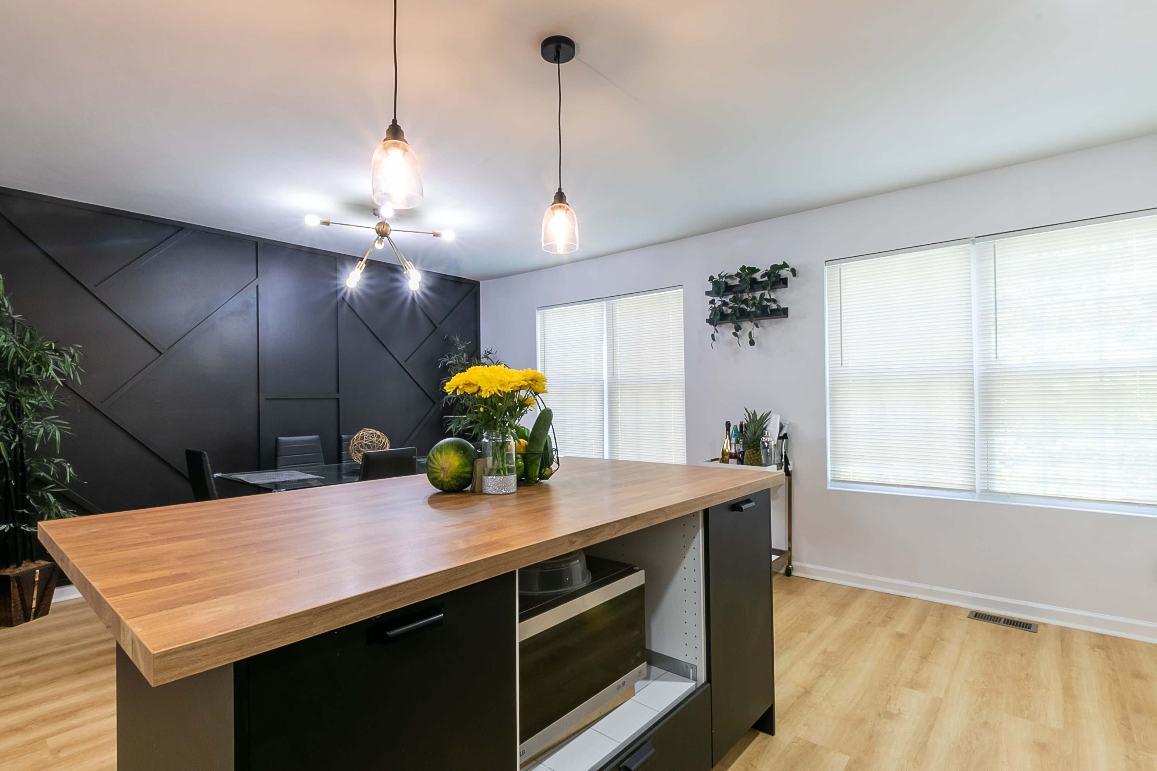 A modern kitchen features a central wooden island with a sleek black base, surrounded by natural light from two windows.