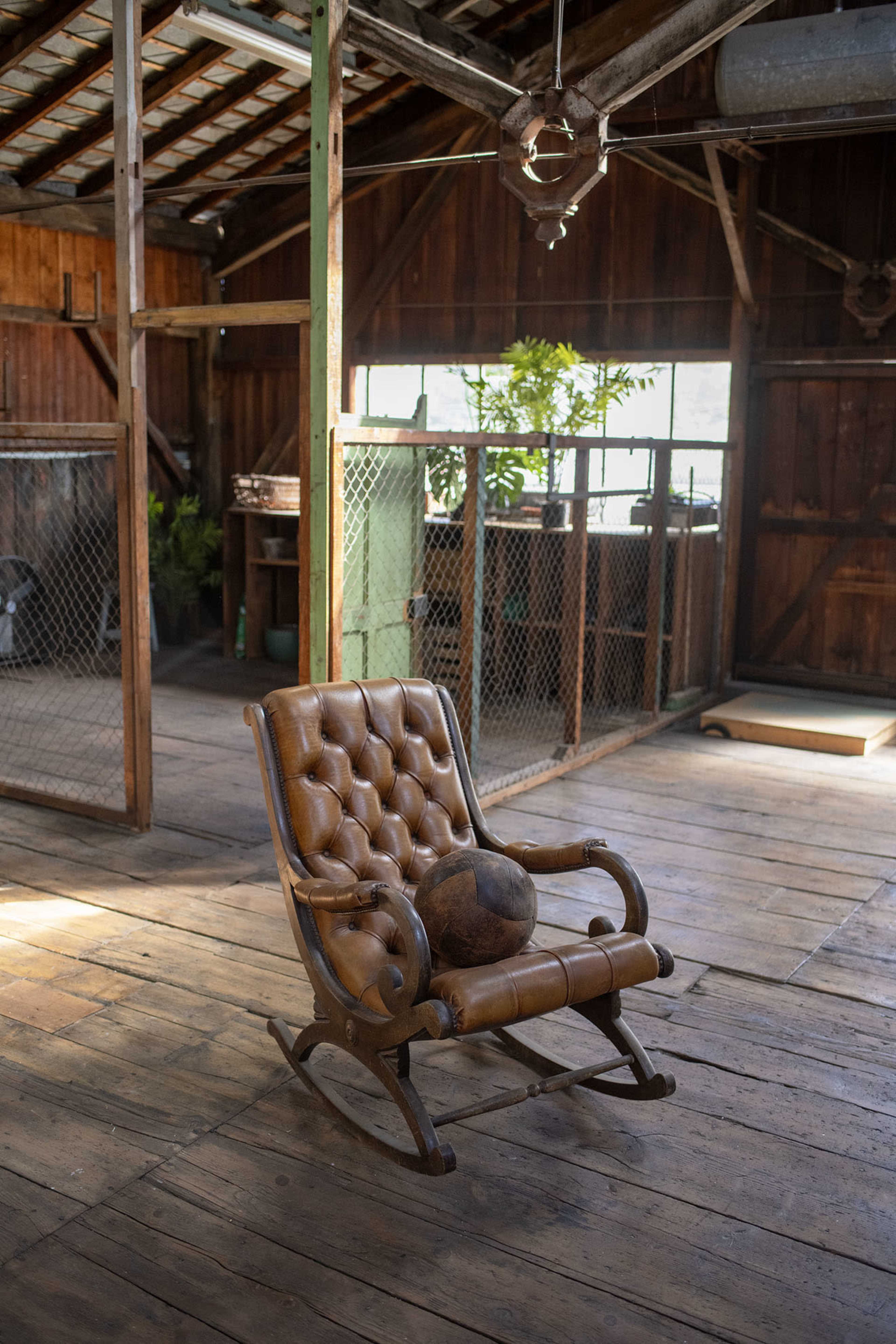 An antique rocking chair sits in a wooden room with exposed beams and a green plant in the background.