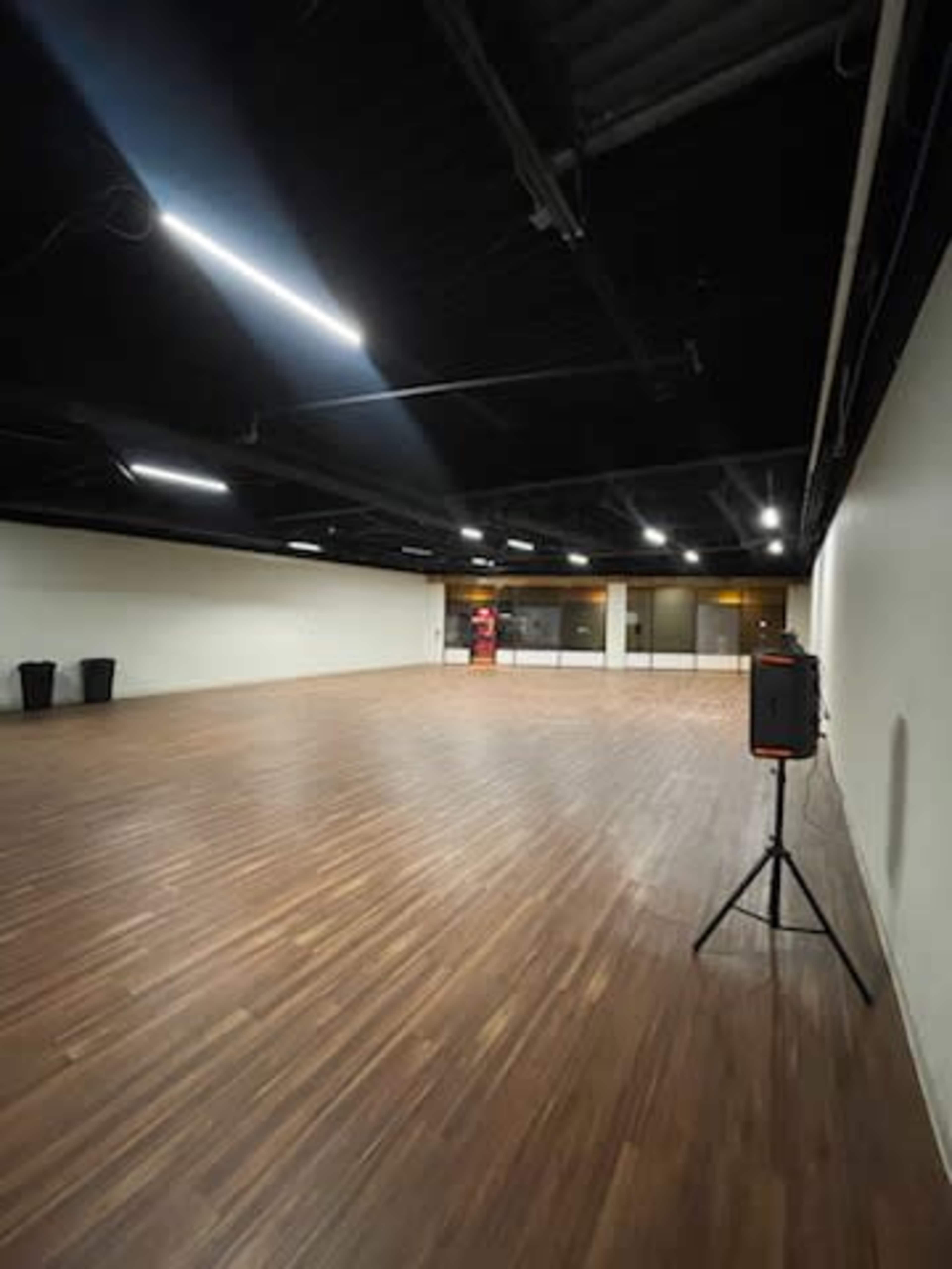 An empty, spacious interior room with wooden flooring, high ceilings, and minimal lighting fixtures.