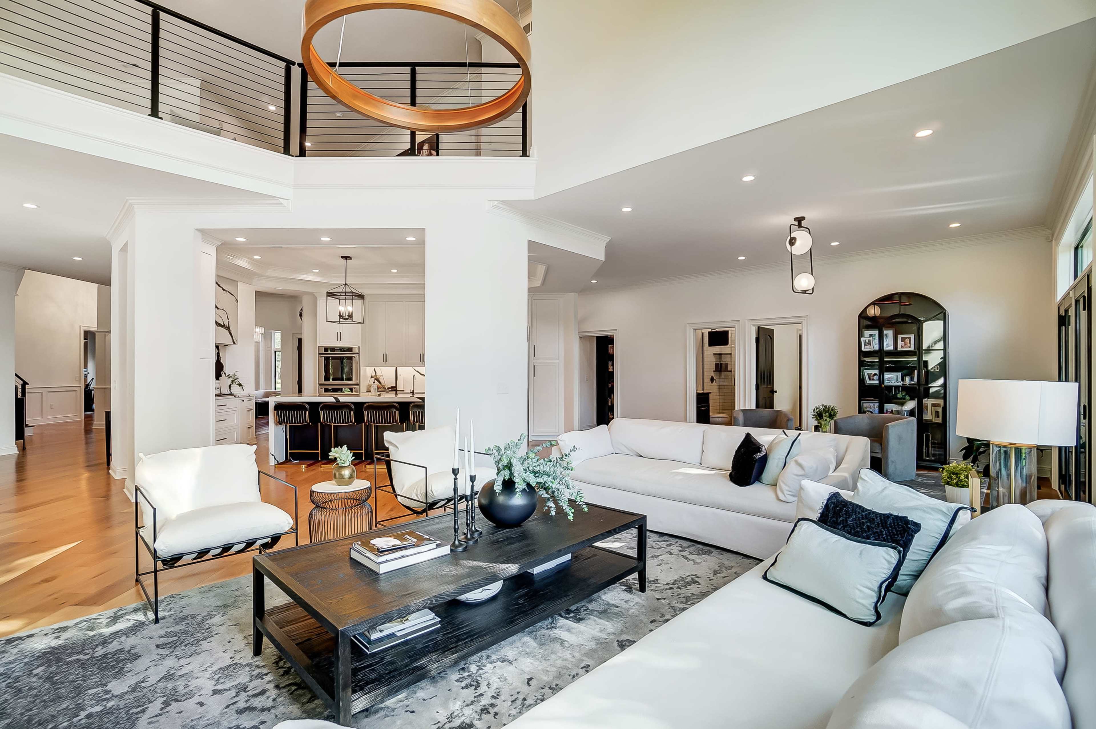 A modern living room with a white sectional sofa, a dark wooden coffee table, and large windows allowing natural light to fill the space.