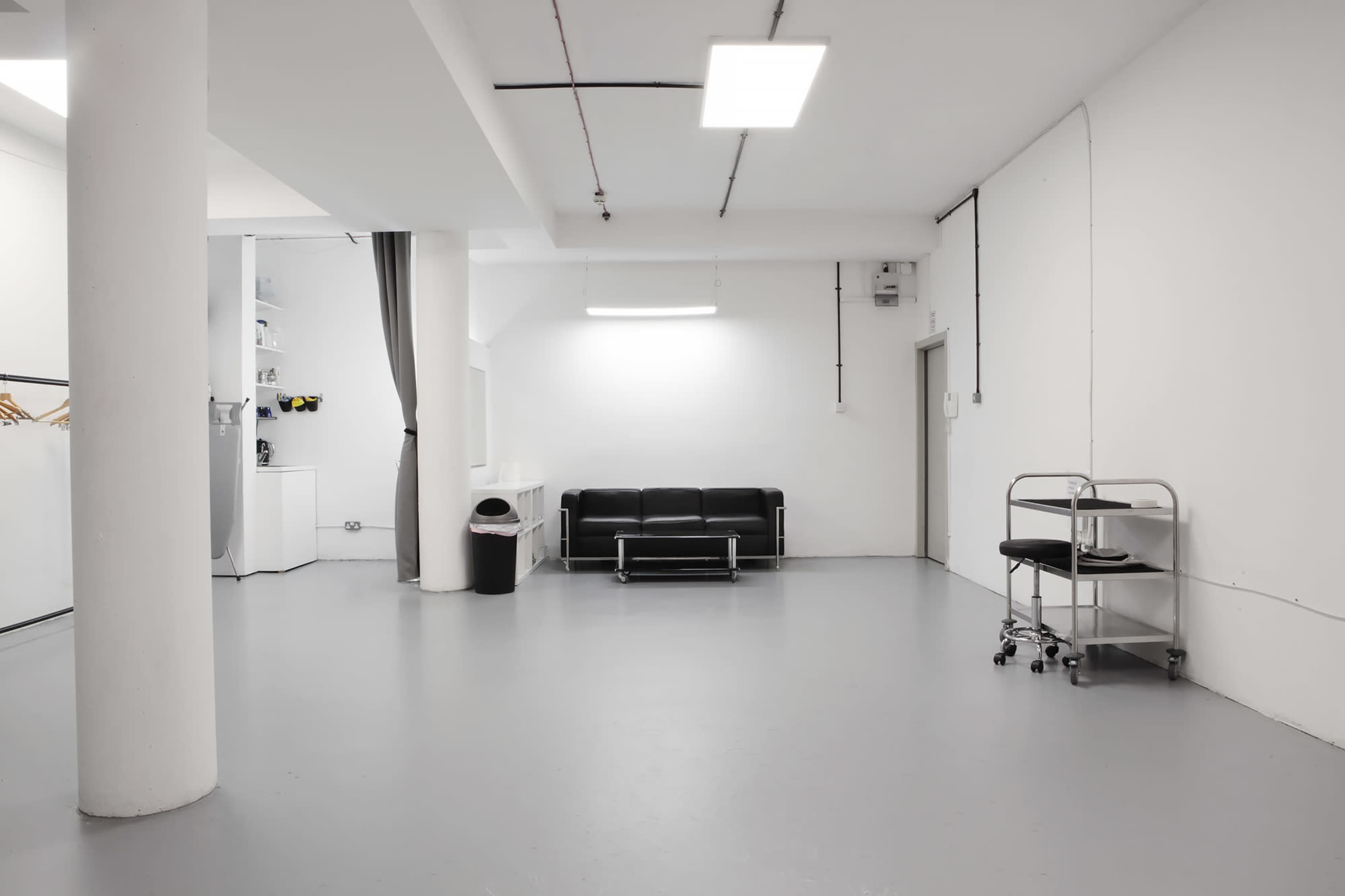 A spacious, minimalist room with a black couch, a metal cart, and light gray flooring.