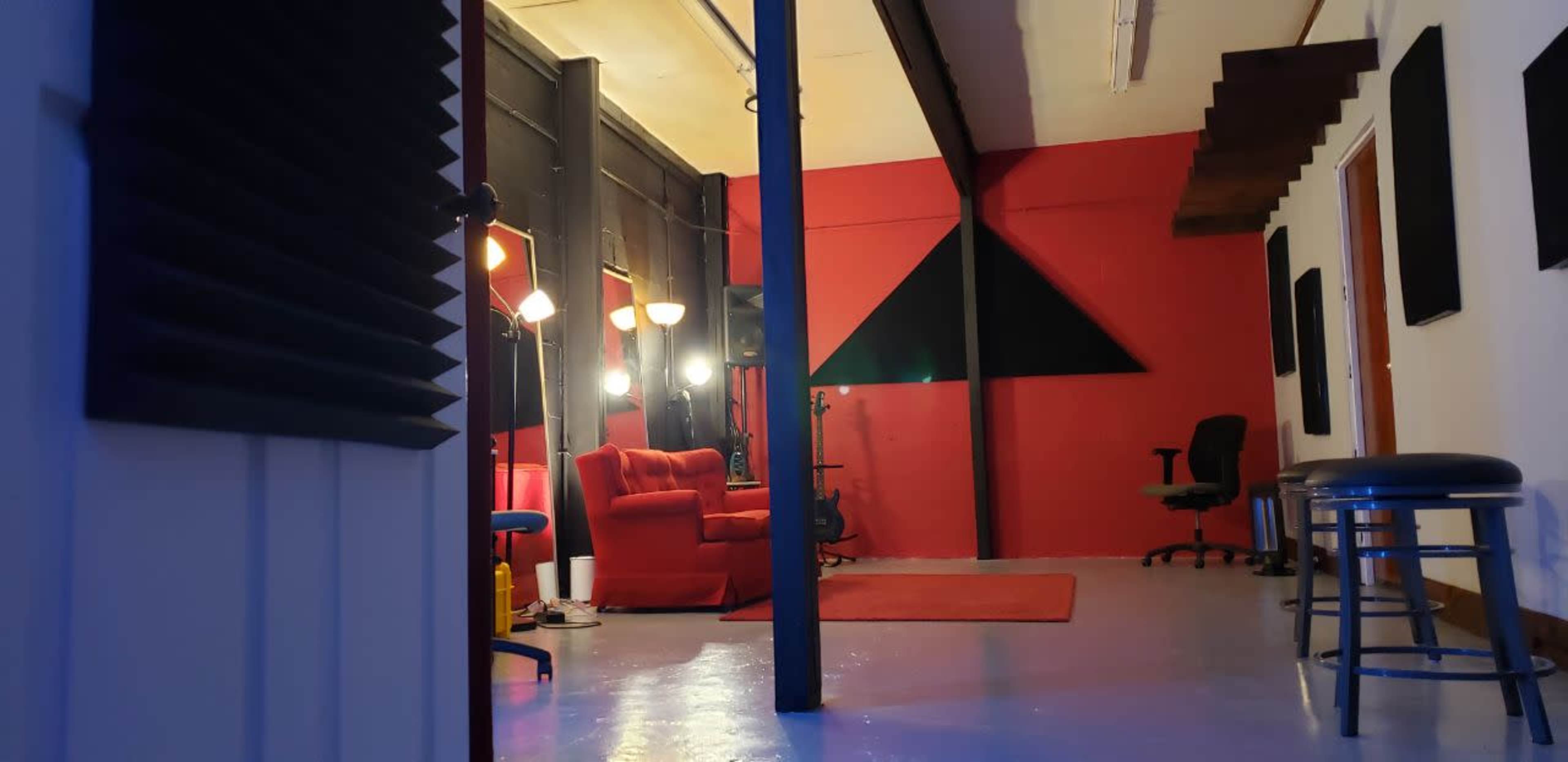 A room with red walls, a red couch, and various lighting fixtures, with chairs and a stool positioned around the space.