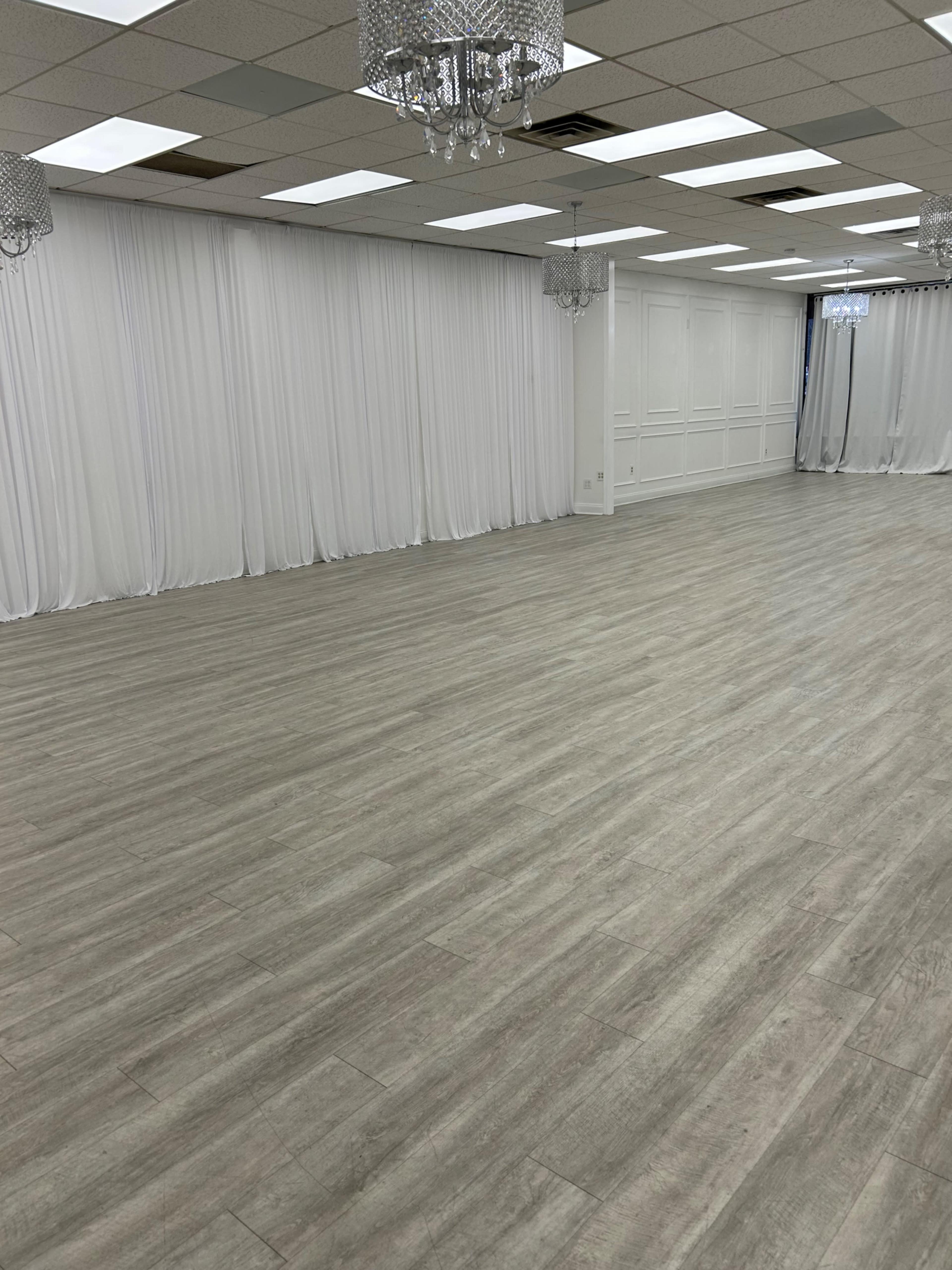 The image shows a spacious room with light-colored wooden floors, white drapes, and several crystal chandeliers hanging from the ceiling.