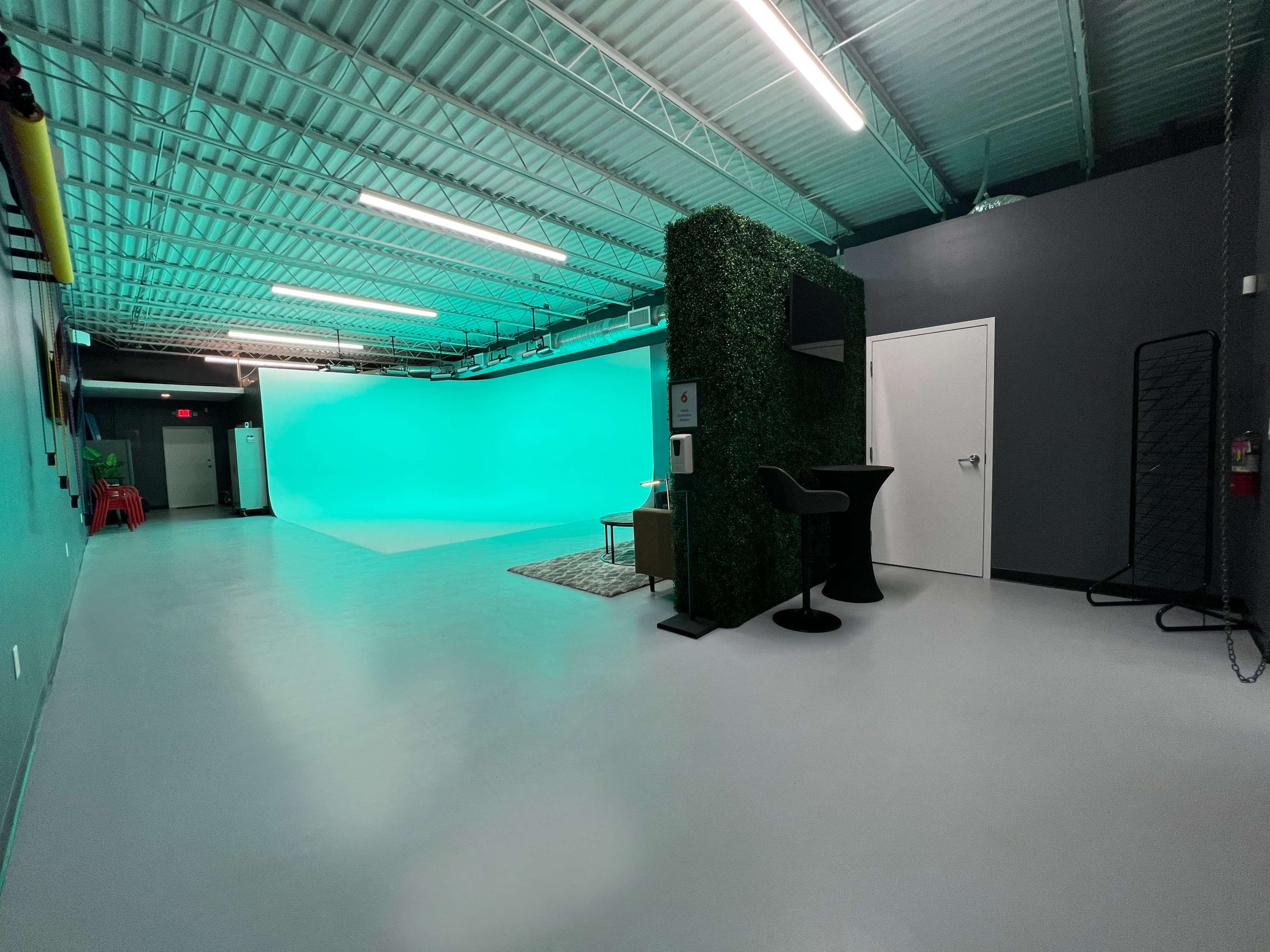 The image shows a spacious studio with a green screen backdrop, a seating area, and a black bar table against a modern gray wall.