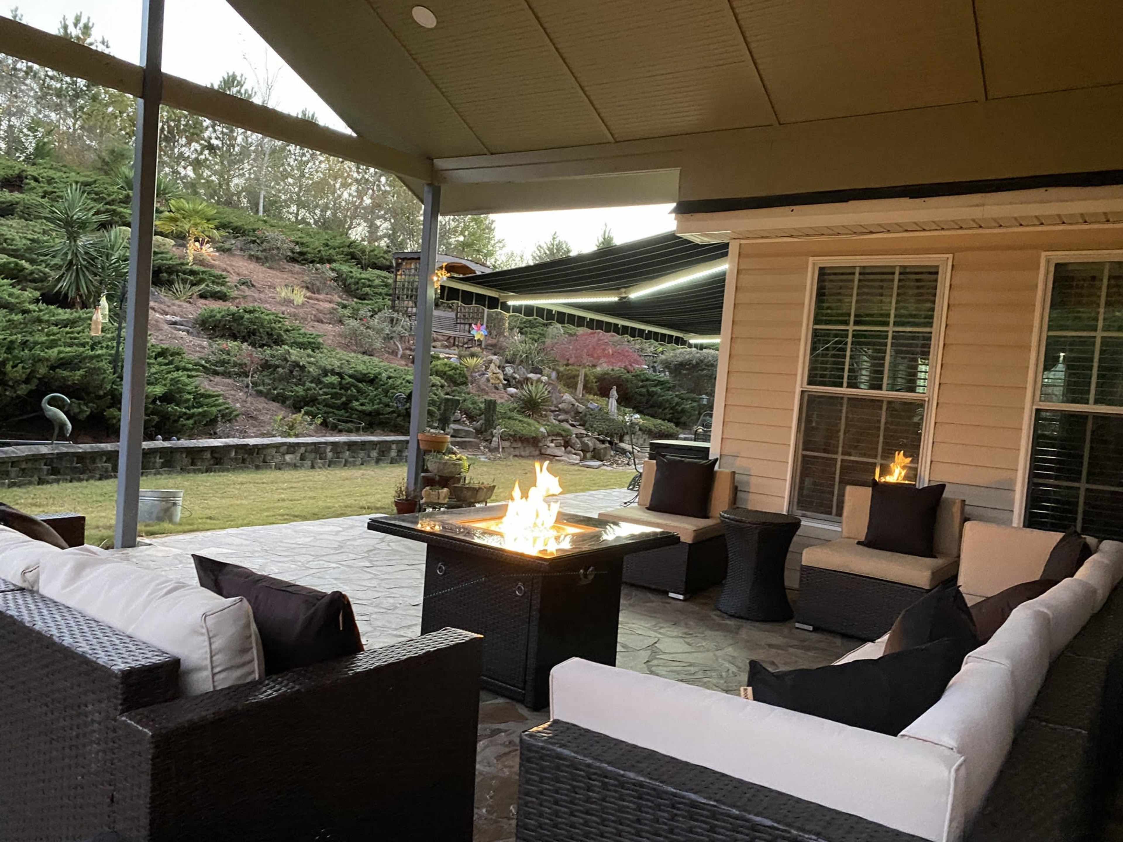 A patio area with seating arranged around a fire pit, surrounded by landscaped gardens and a sloped hillside.