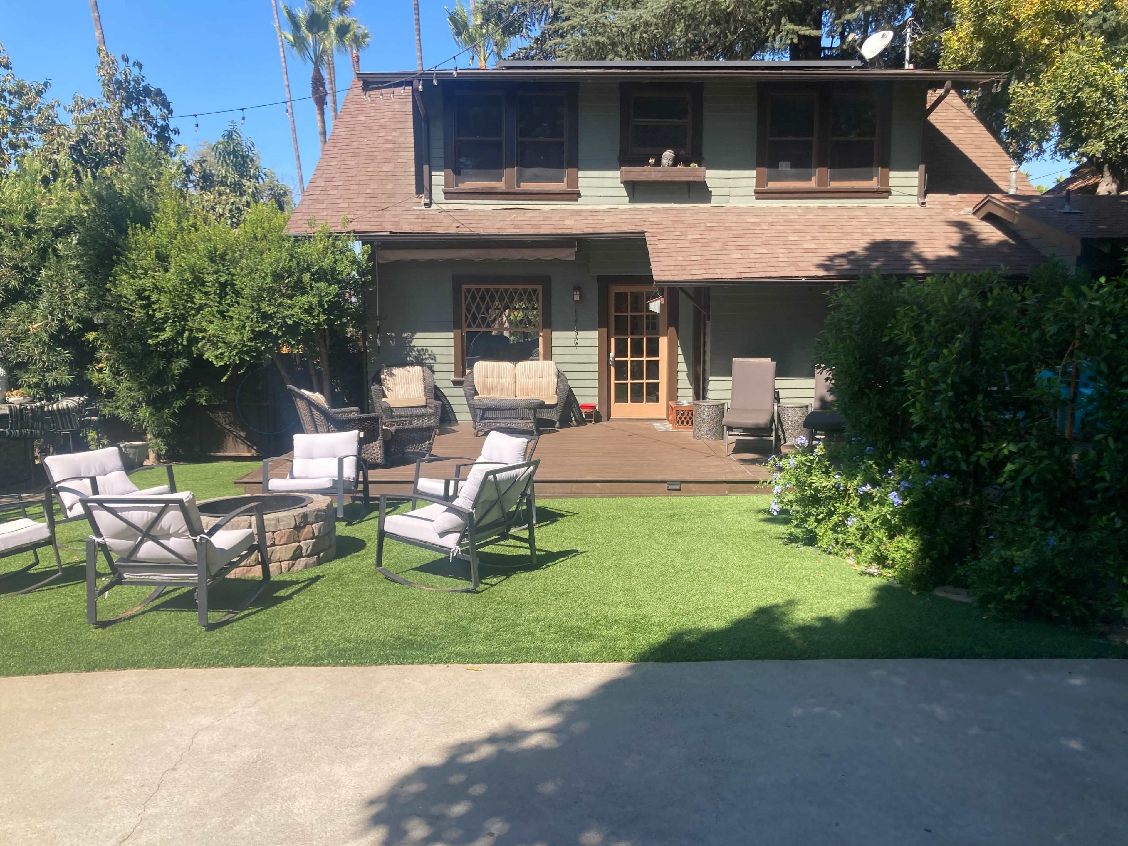 The image shows a backyard scene with a deck and outdoor seating arrangement in front of a two-story house.