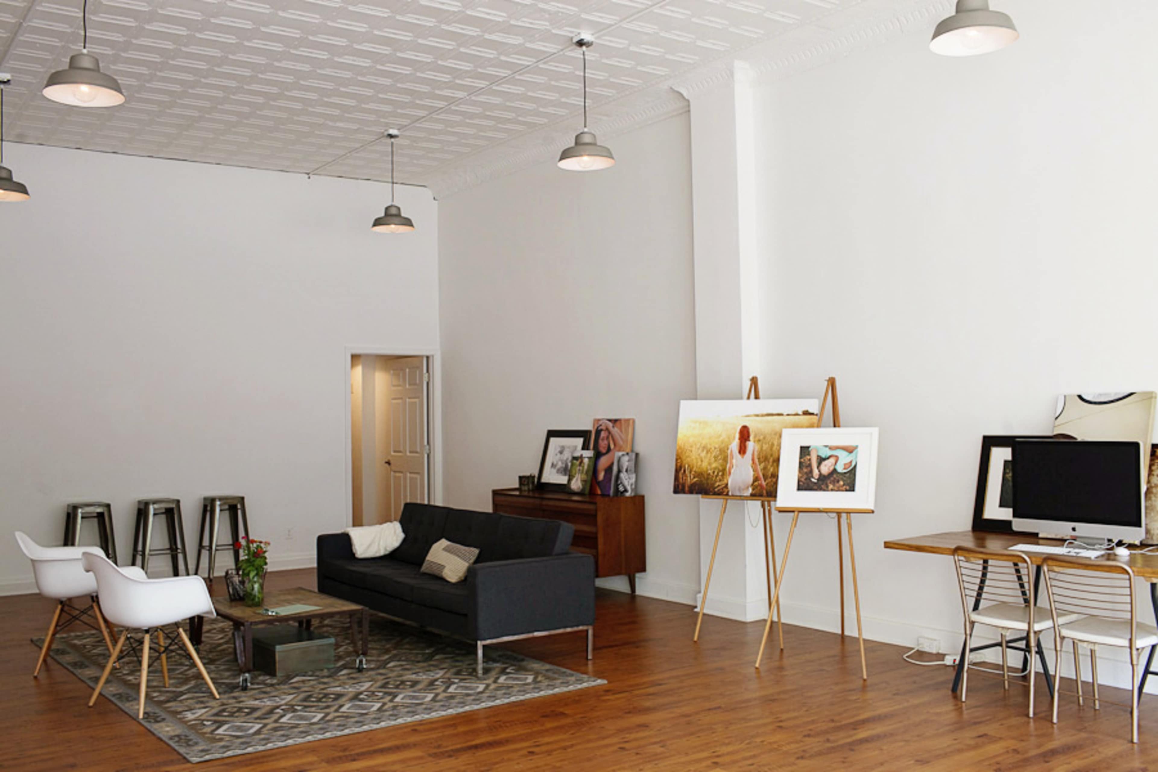 A spacious, modern interior with a couch, wooden furniture, and artwork displayed on easels.