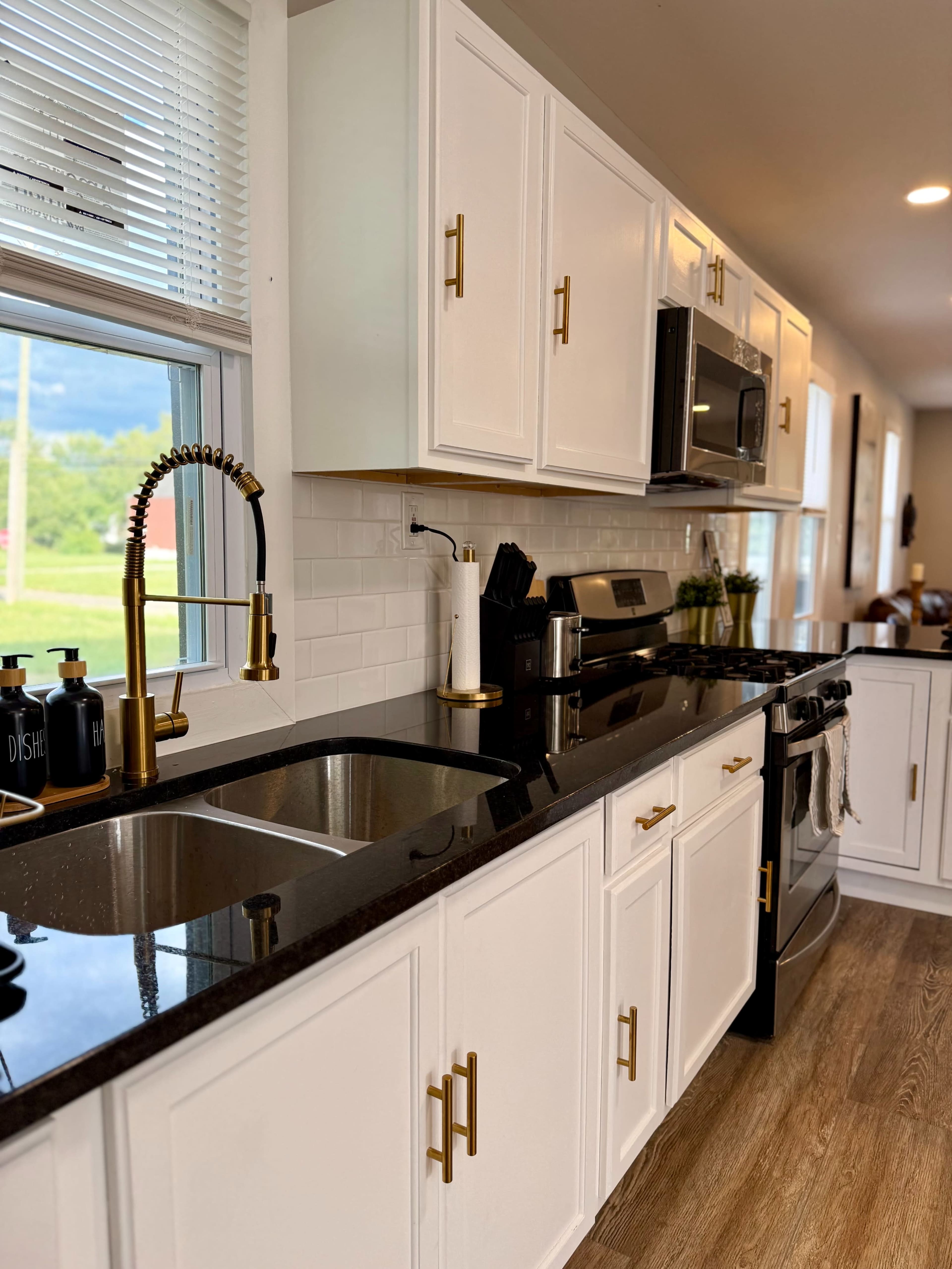 The image shows a modern kitchen with white cabinetry, a black granite countertop, and gold hardware, featuring a stainless steel microwave and a gas stove.
