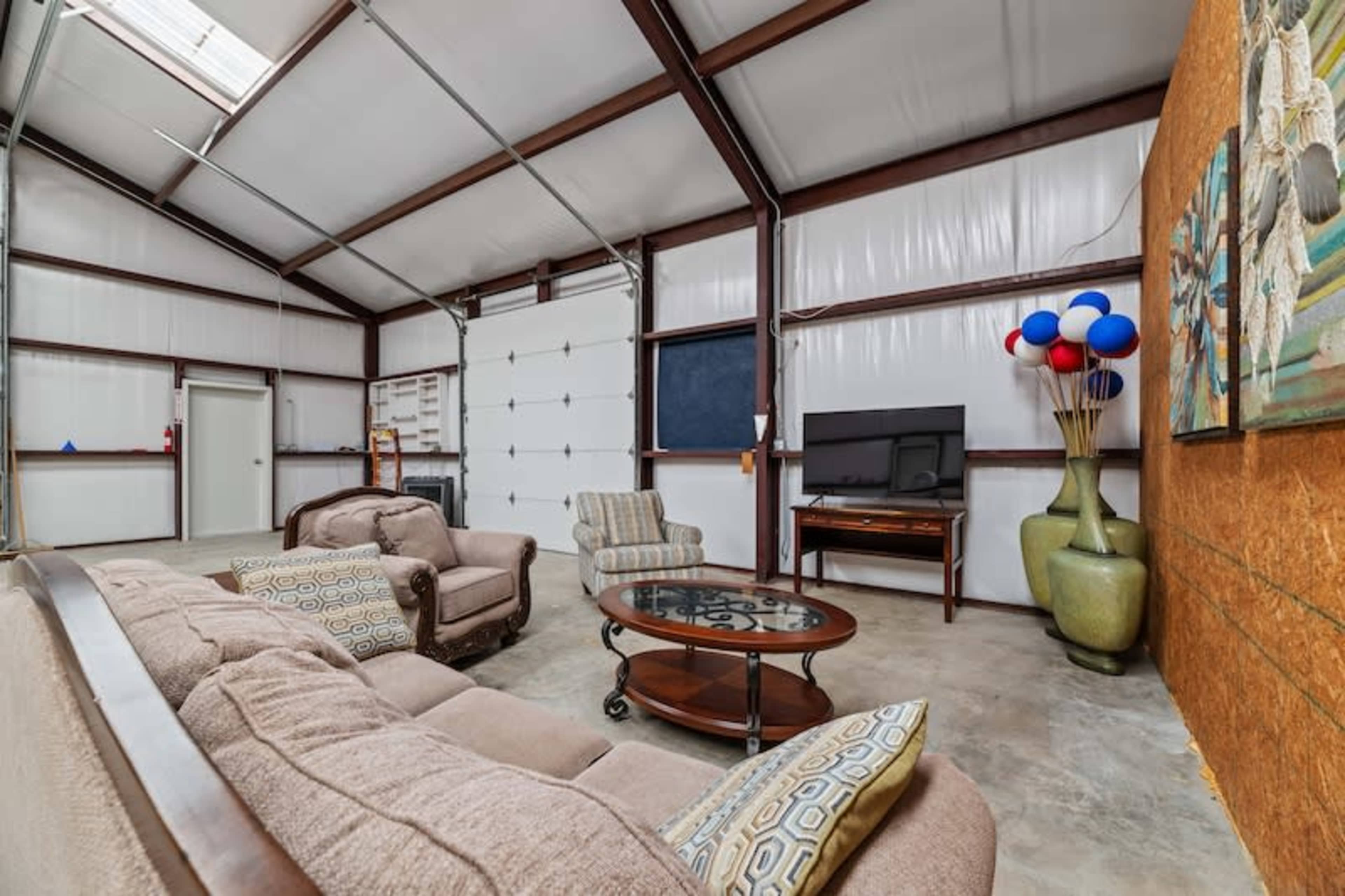 A spacious interior of a metal building with a seating area, a television, and decorative elements like a vase and balloons.
