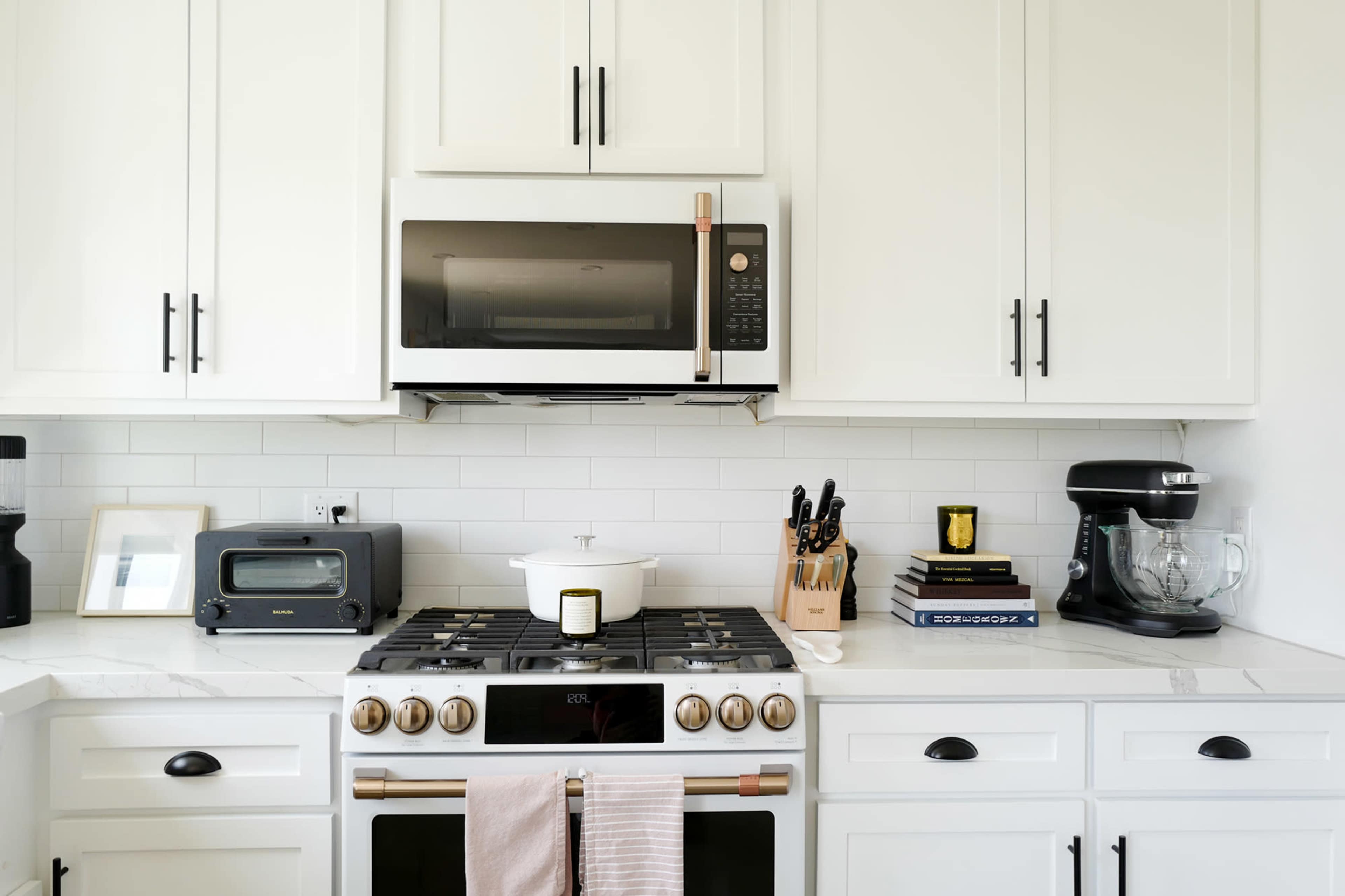 A modern kitchen with white cabinetry, a stainless steel microwave above a gas stove, and various kitchen appliances and tools arranged on the countertop.