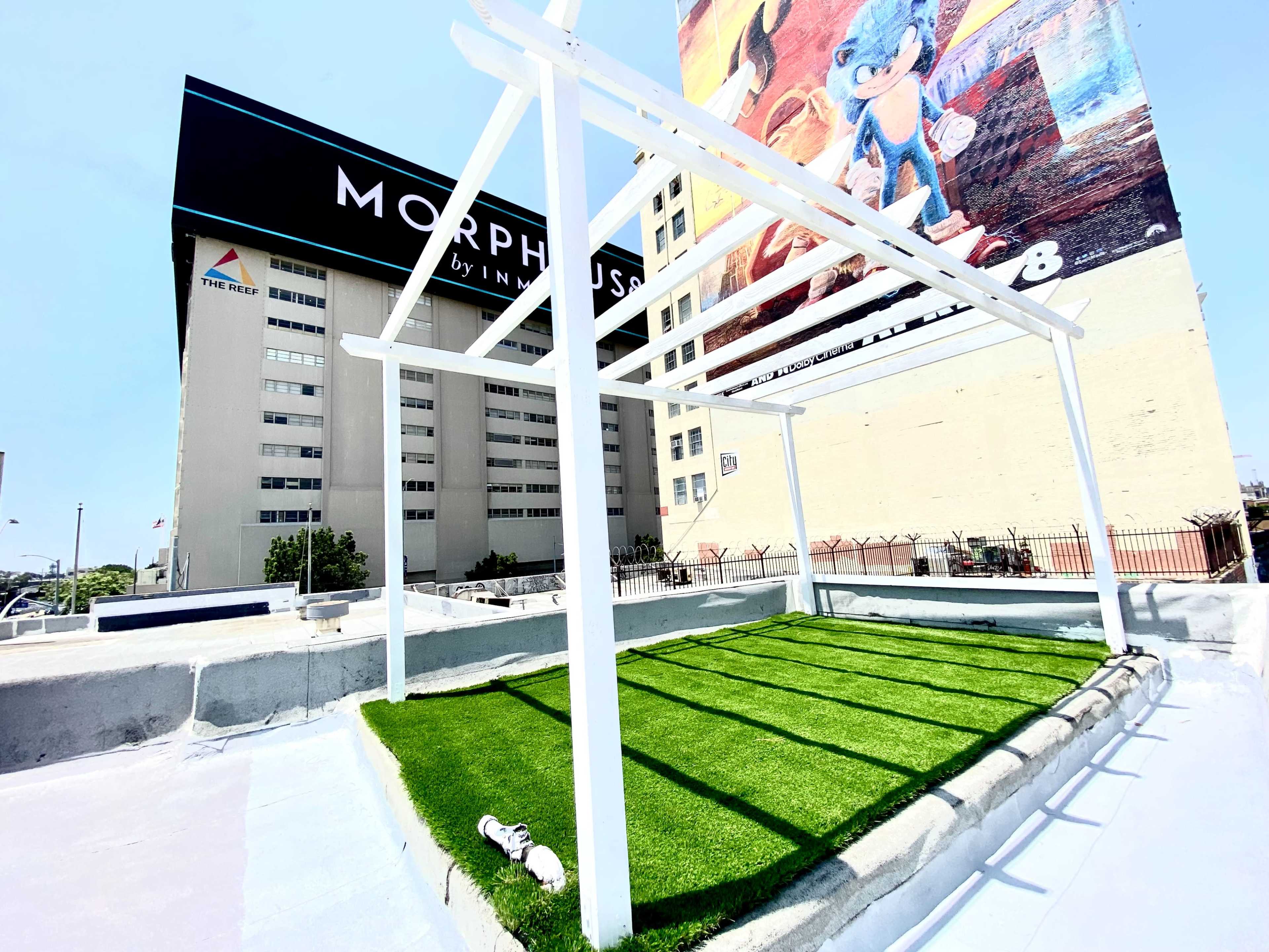 A rooftop space with a green artificial lawn and a white framework, set against a large mural featuring a cartoon character.