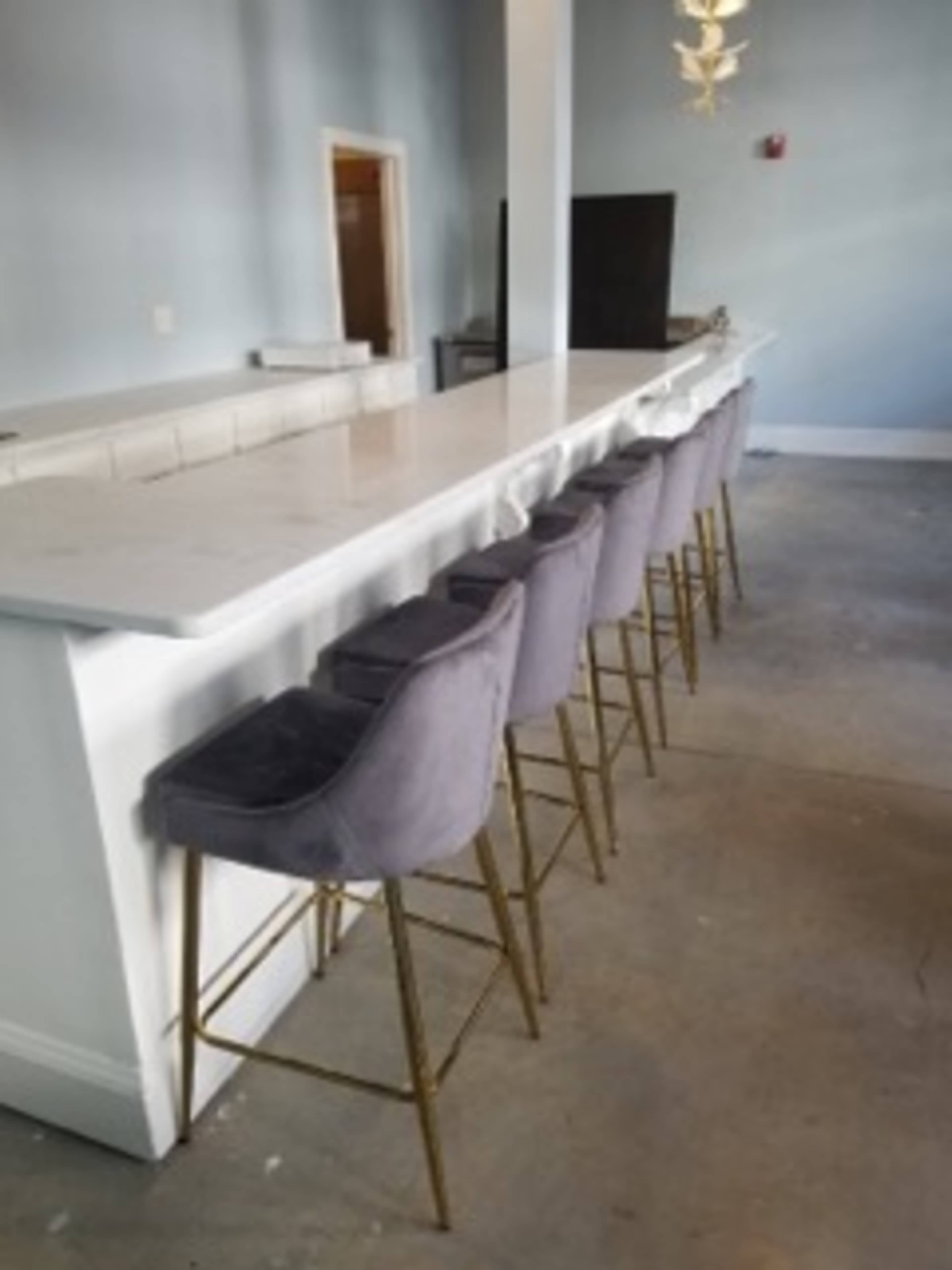 A row of gray upholstered bar stools is lined up against a white marble countertop in a brightly lit room.