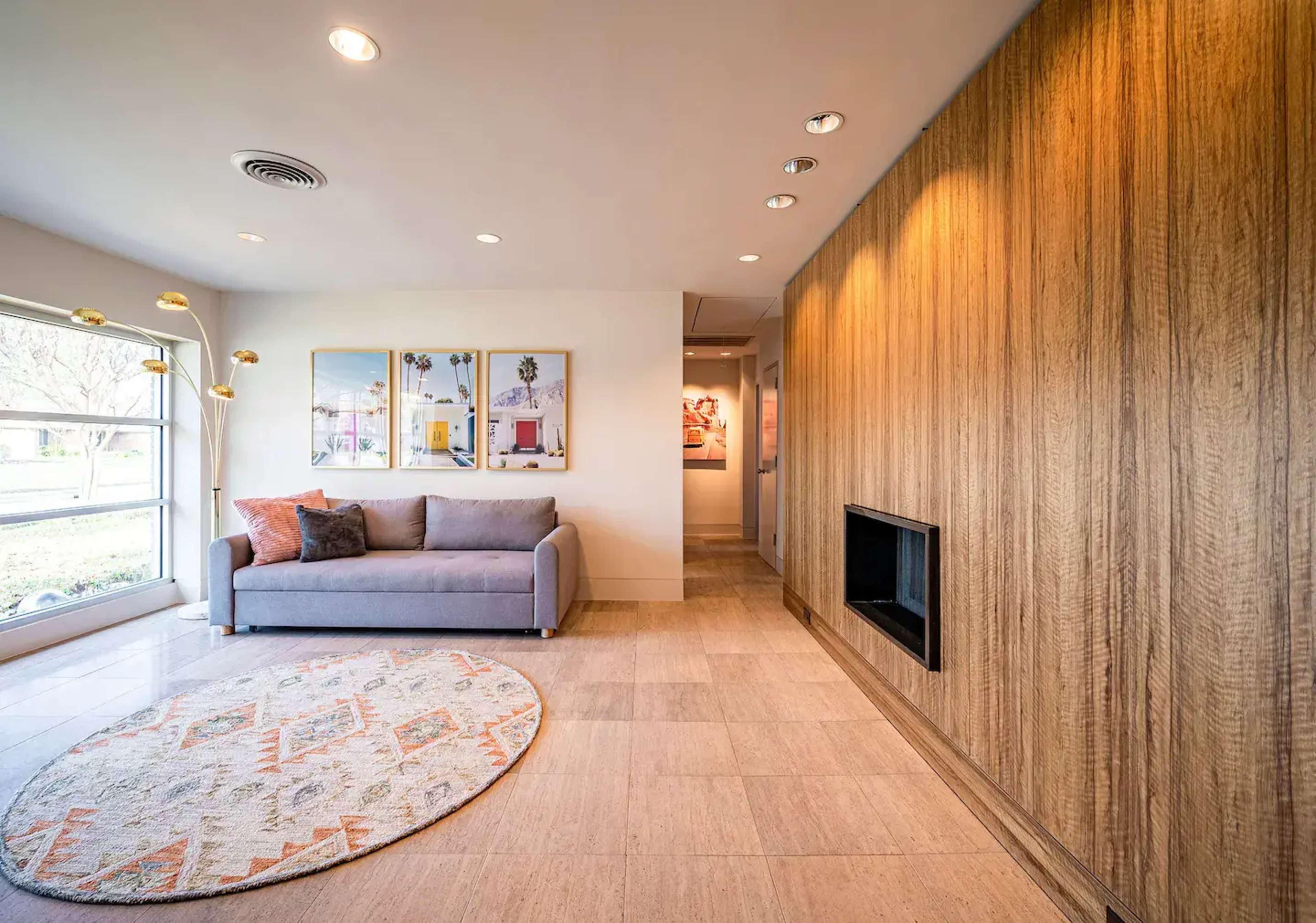 A modern living room with a gray sofa, a round area rug, two framed pictures on the wall, and a warm wooden accent wall.