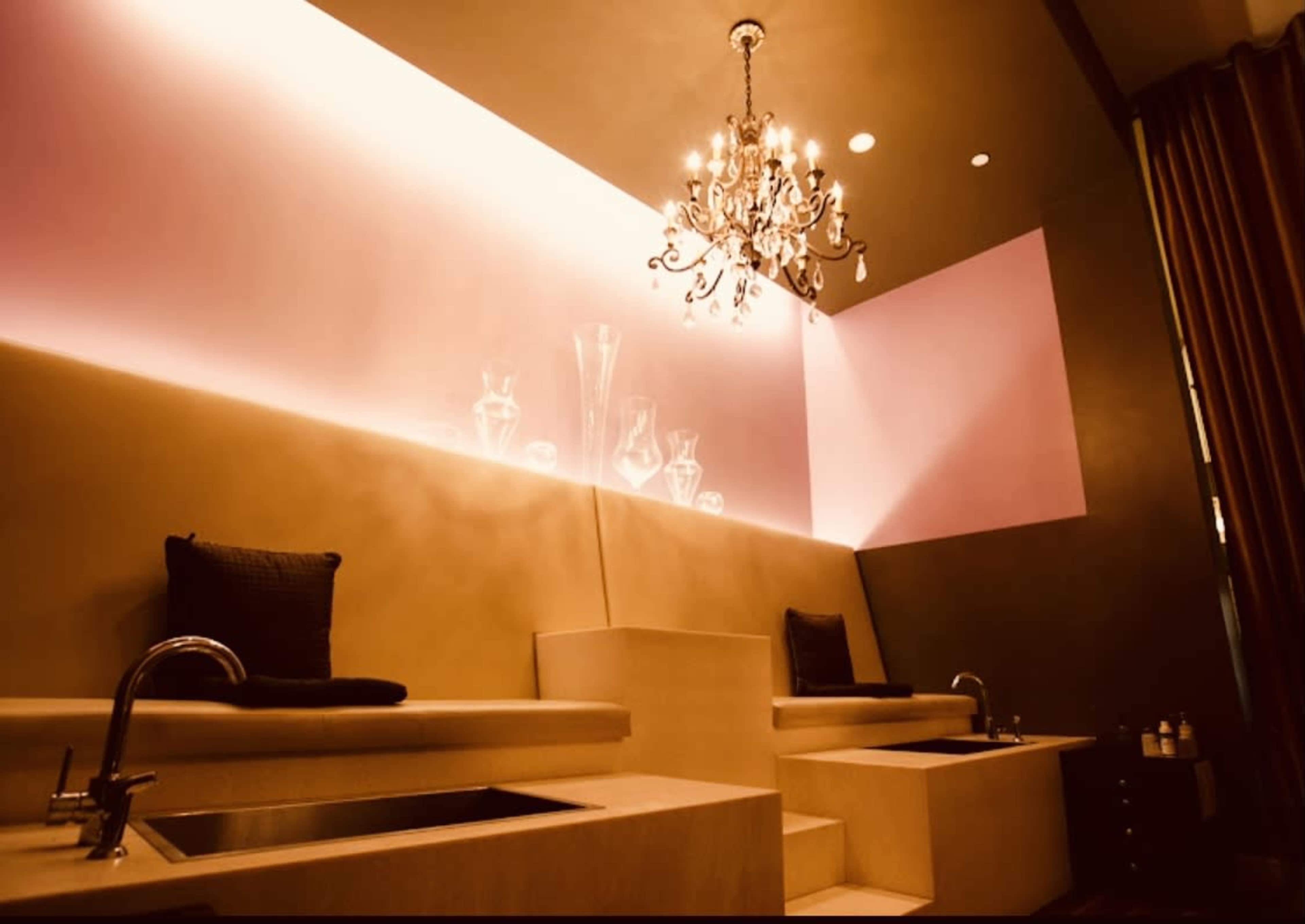 A serene spa interior with two elevated lounge areas, each featuring a sink, and illuminated by a chandelier above.