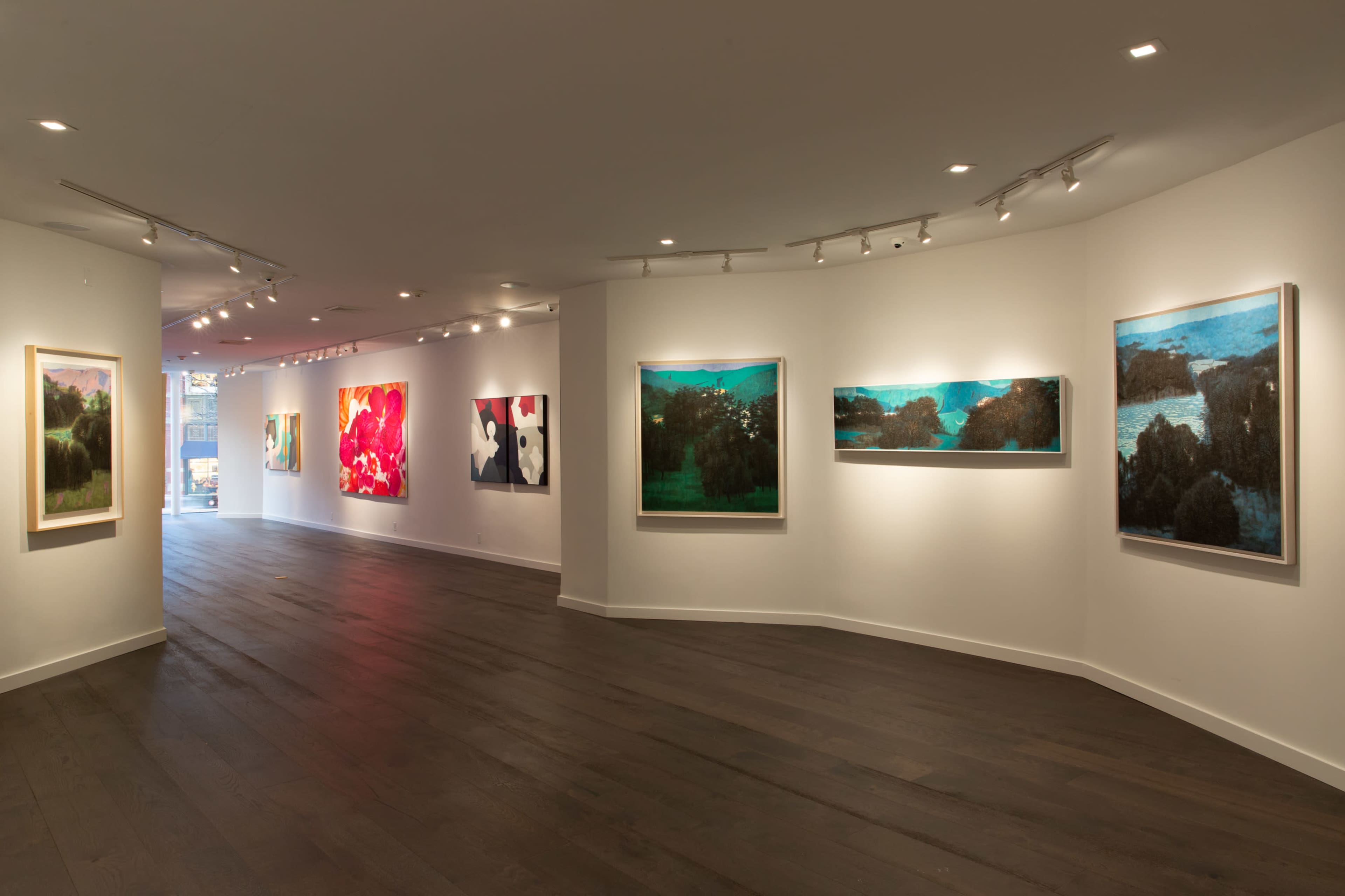 A gallery interior with several framed artworks displayed on white walls and light hardwood flooring.