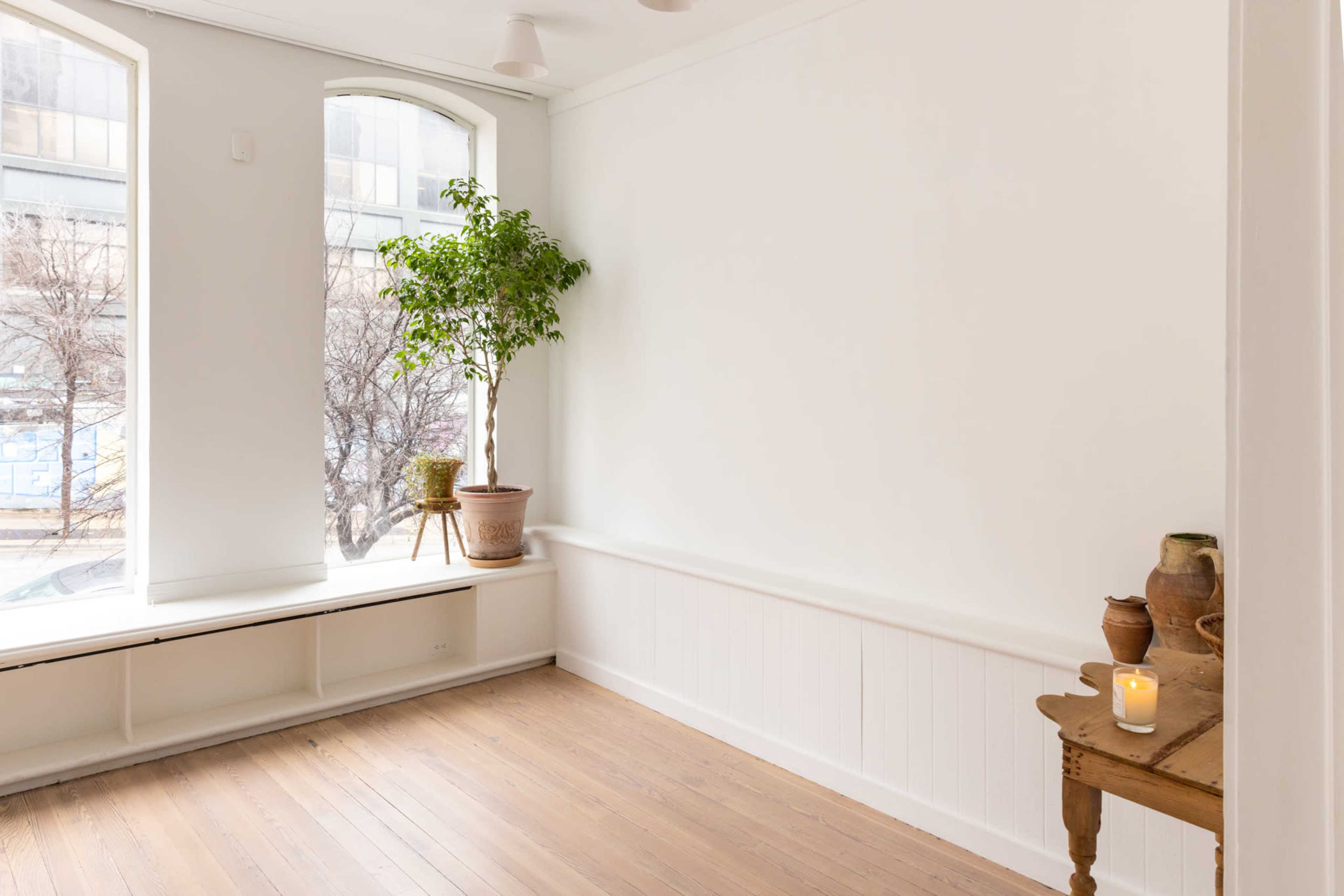 A light-filled room with a large window, a potted plant in the corner, and a wooden table with a candle and decorative items.