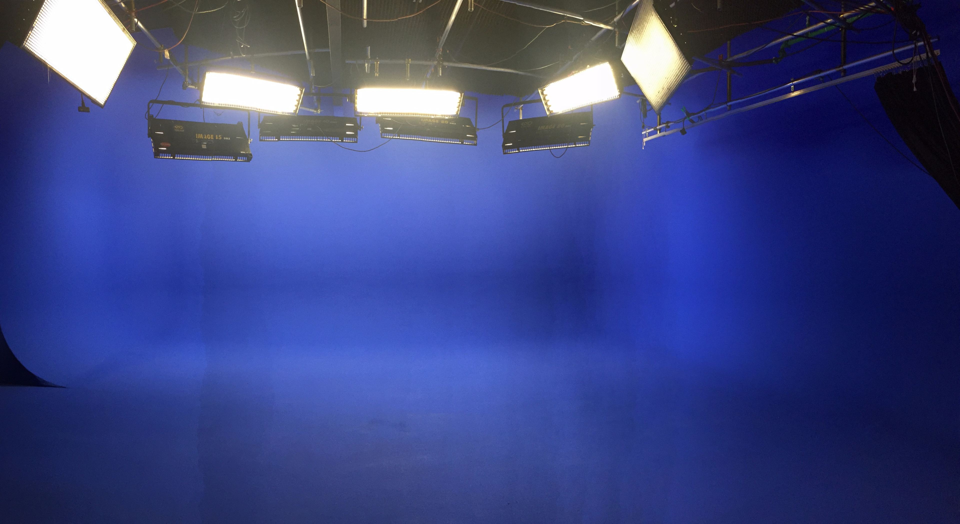 The image shows a studio setup with four bright lights positioned above a blue backdrop.