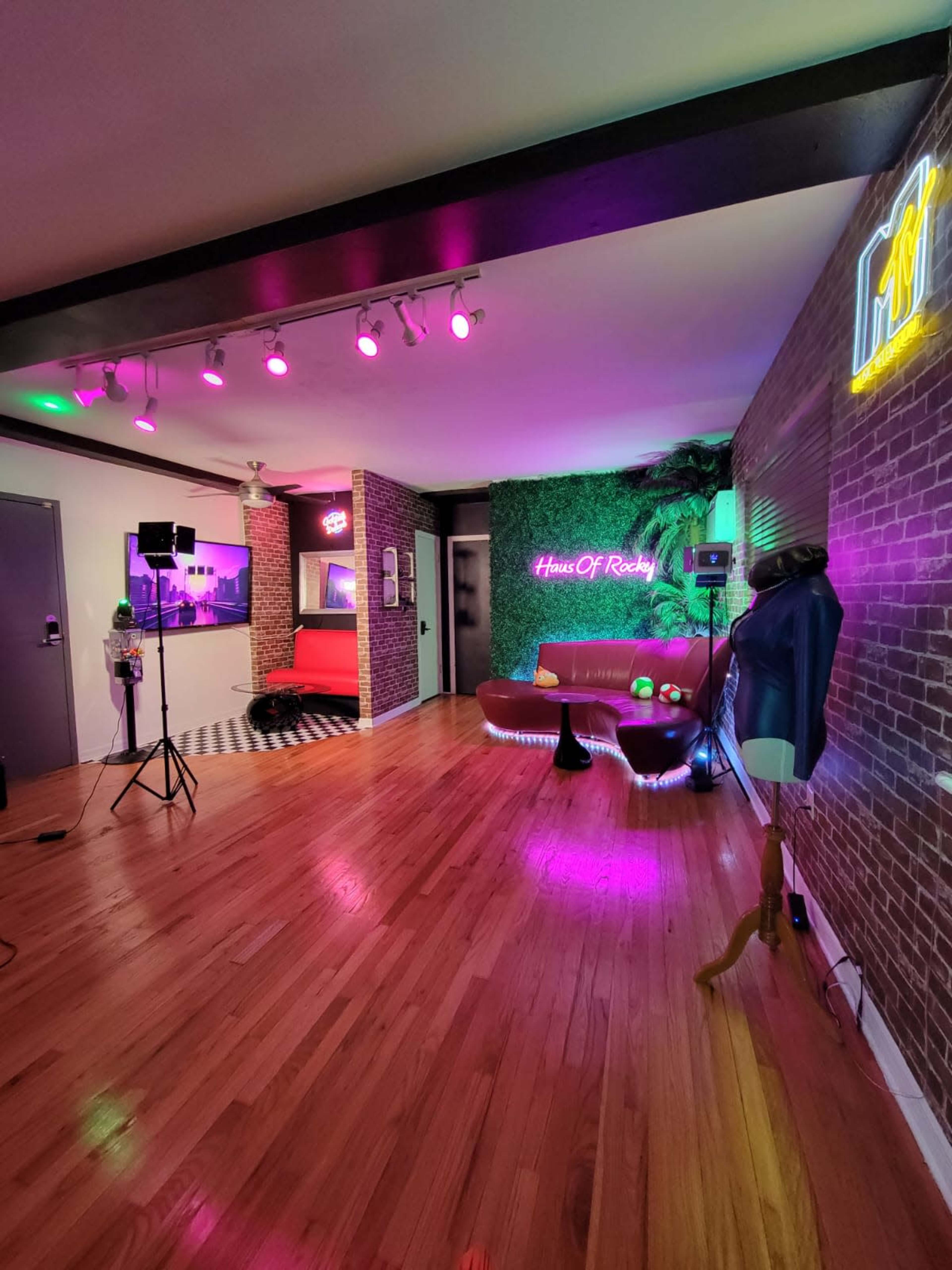 A modern room featuring hardwood floors, colorful lighting, a red couch, and decorative elements like plants and neon signs.