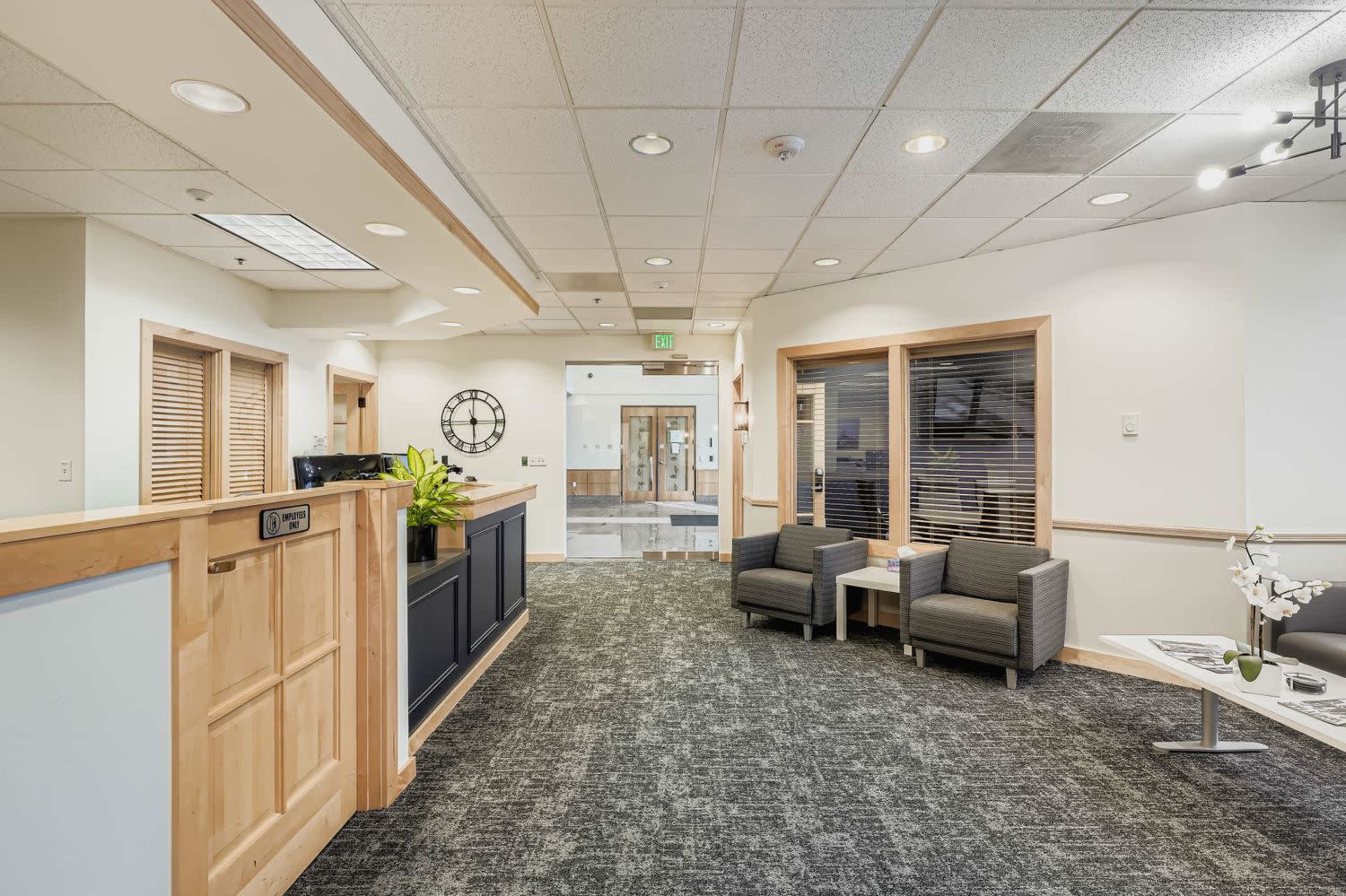 The image displays a modern reception area featuring a front desk, seating, and large windows with natural light.