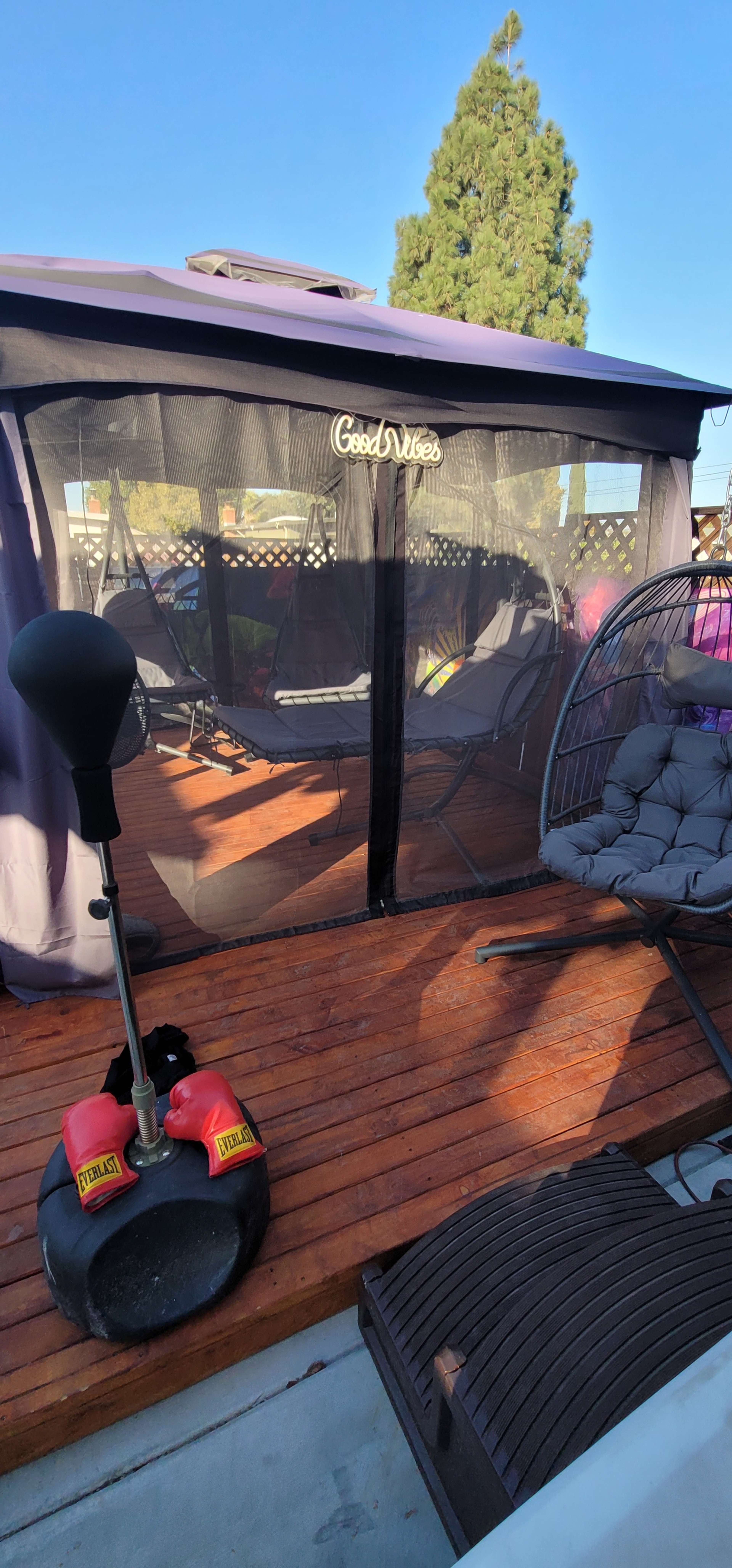 A gazebo with seating areas, including a hanging chair and swings, is set on a wooden deck surrounded by trees.