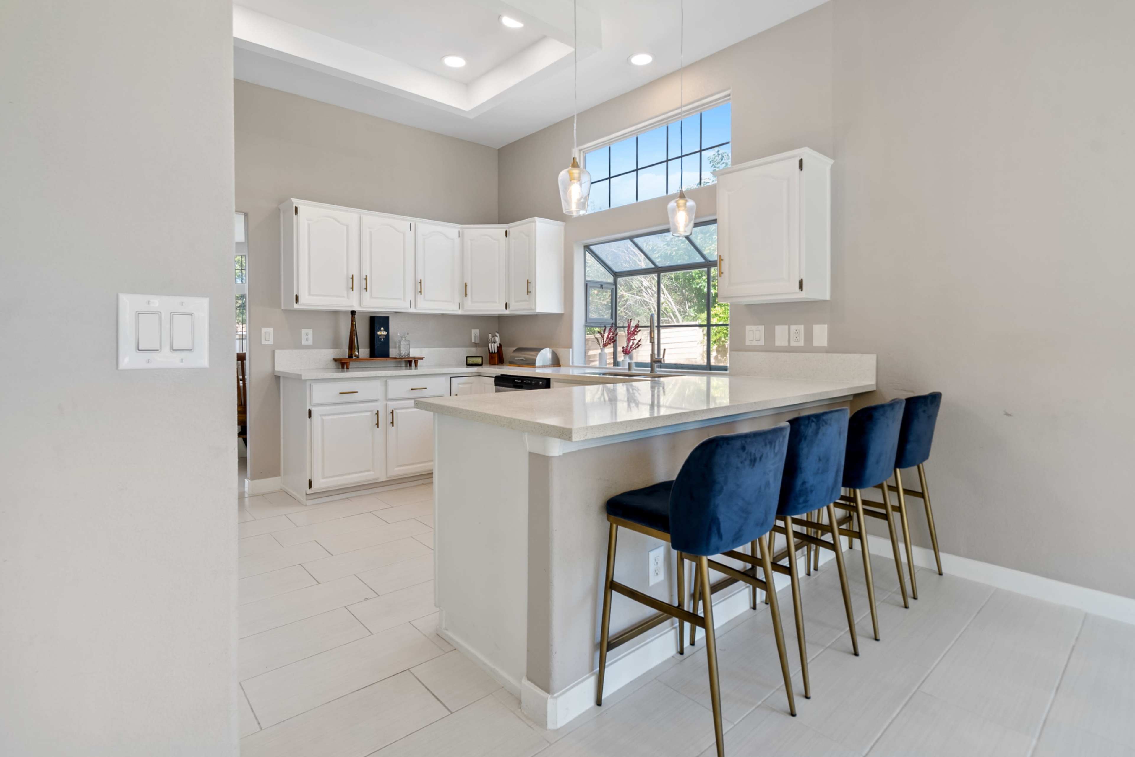 A modern kitchen features white cabinetry, a large island with bar seating, and a window allowing natural light to illuminate the space.