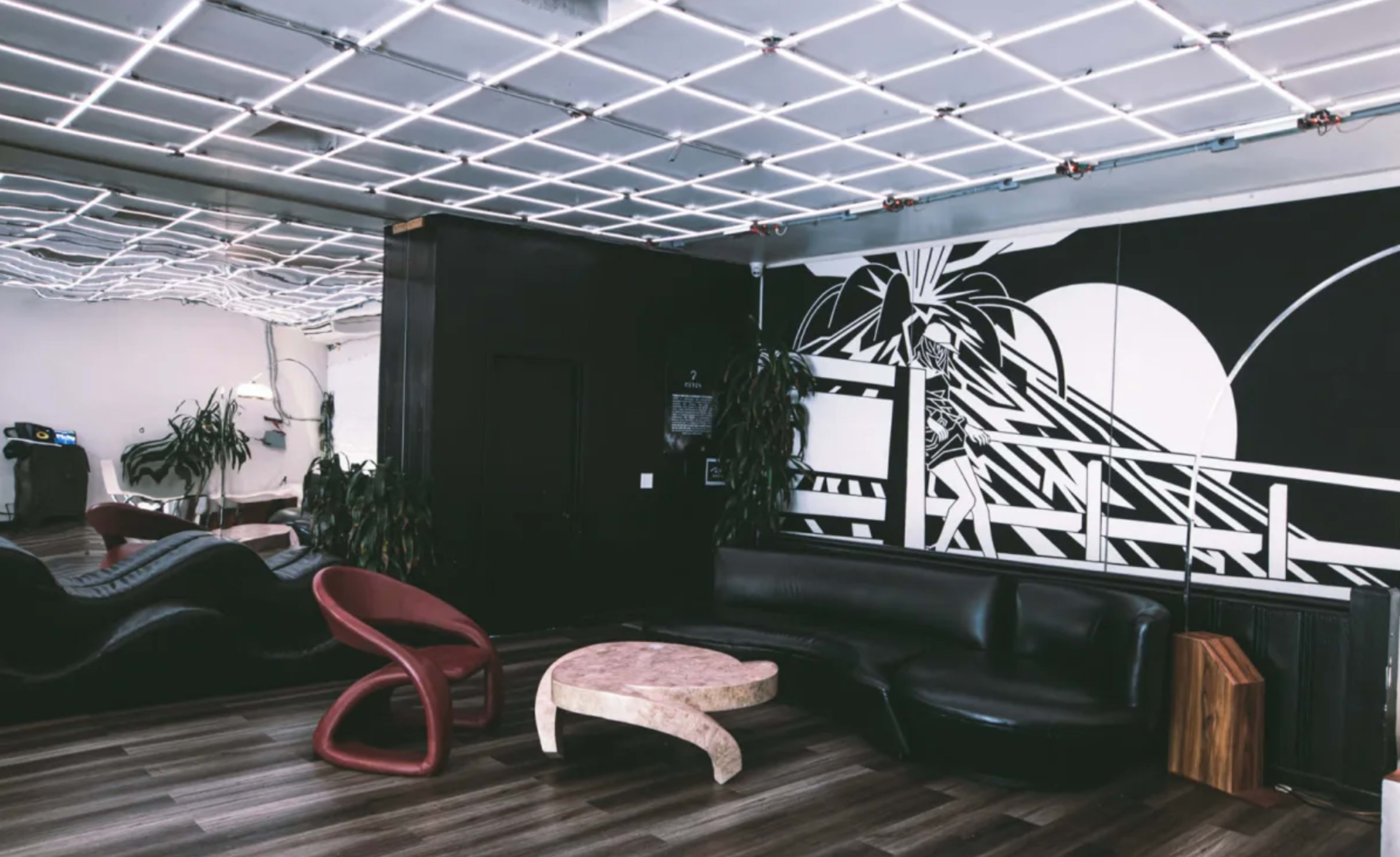 A modern lounge area with a patterned ceiling, a large black couch, a marble coffee table, and a mural on the wall.