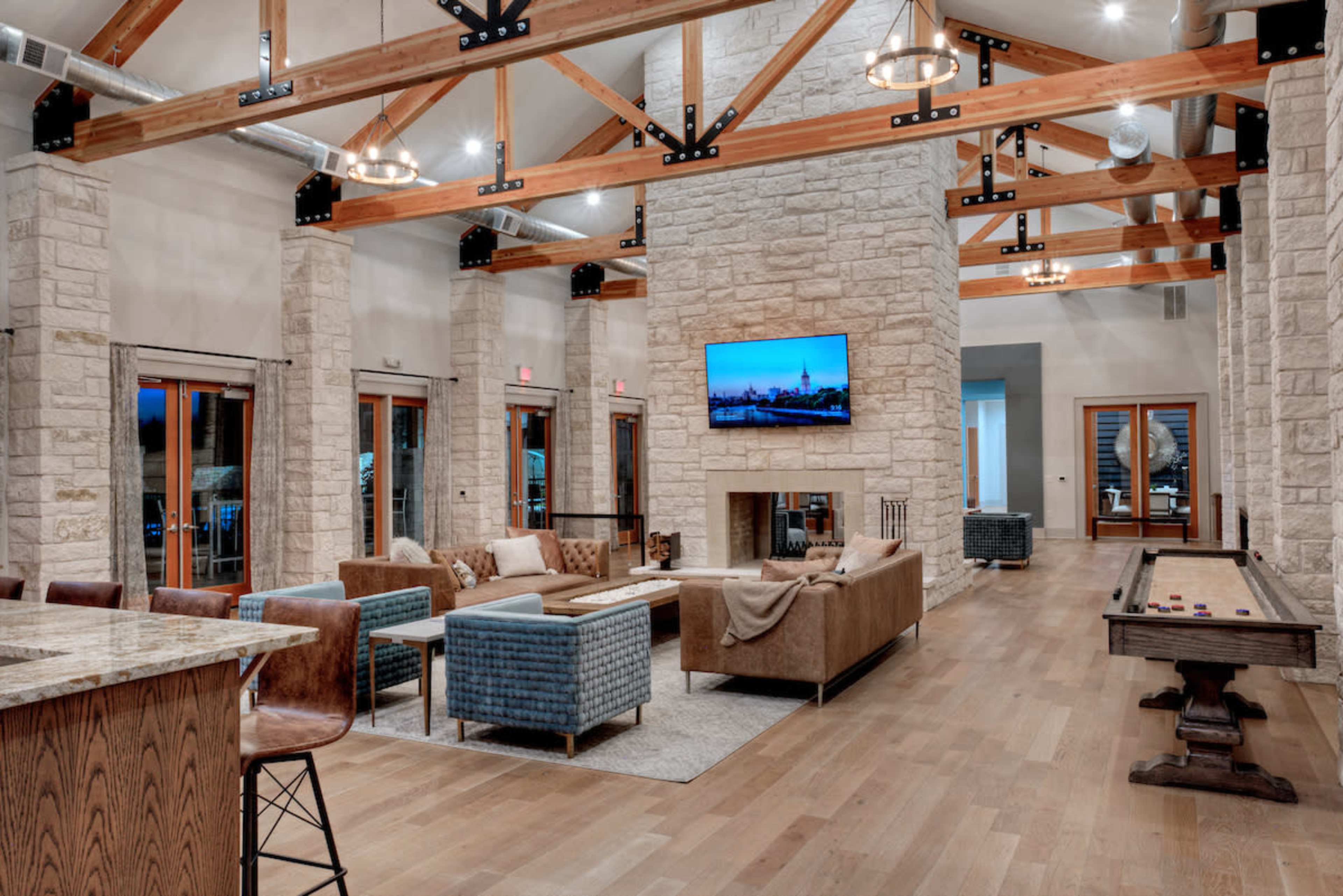 A spacious interior lounge area with stone walls, wooden beams, and a large television mounted above a fireplace, accompanied by comfortable seating arrangements and a pool table.