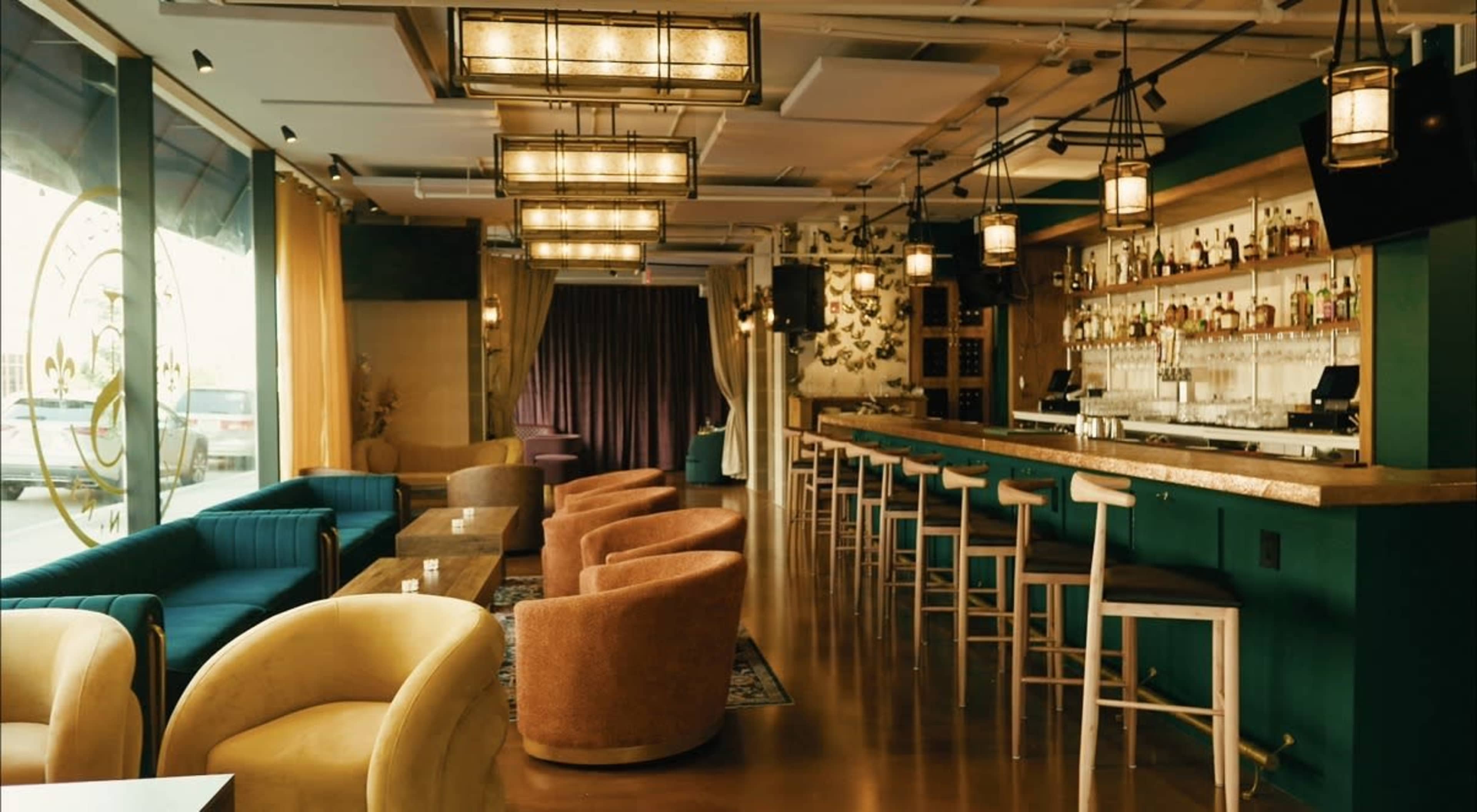 The image shows a modern lounge bar with colorful seating, a polished wooden bar counter, and ambient lighting.