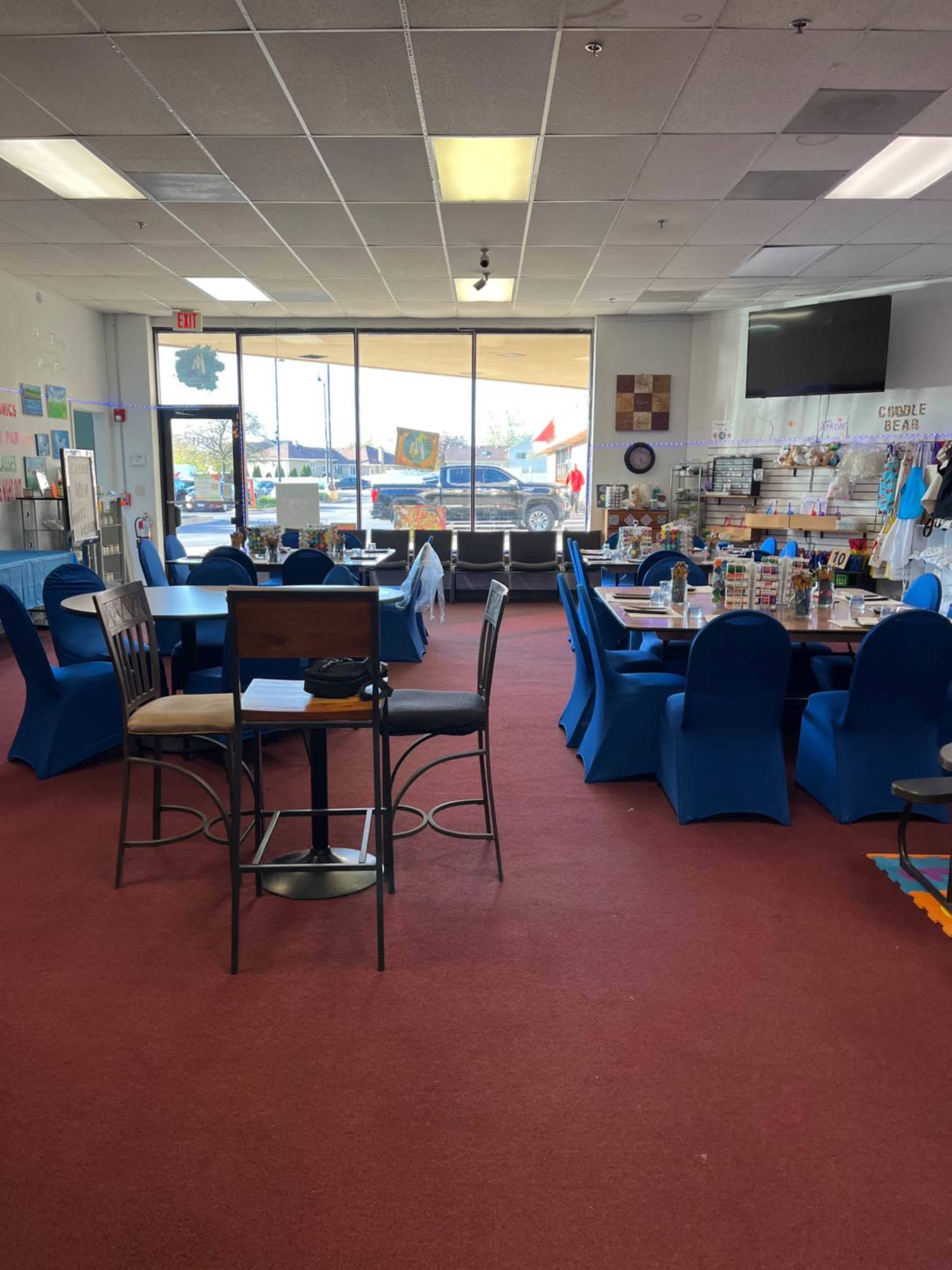 A brightly lit room with blue covered tables and chairs, along with a large window facing the street.